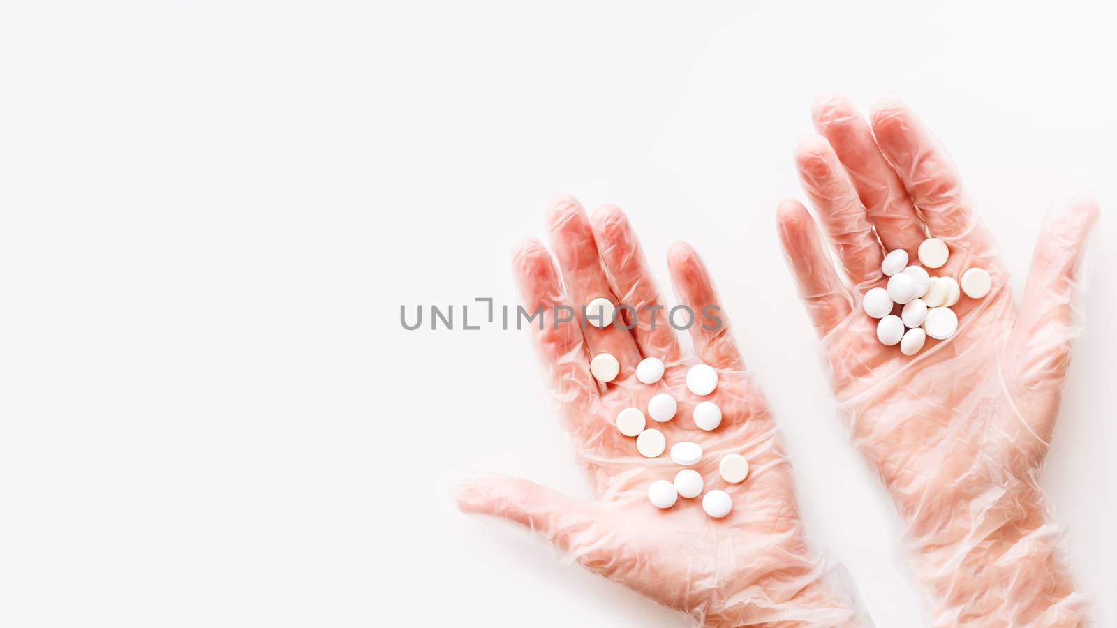 Doctor's palm hands in protective transparent gloves full of white scattering pills. Capsules with medicines on white background with copy space. Flat lay, top view.