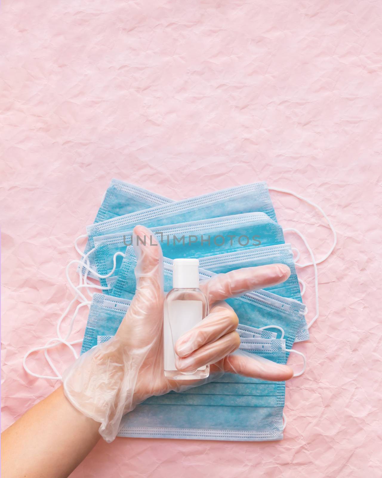 Top view on hand in protective gloves with medical masks and sanitizer in transparent bottle. Woman make victory gesture. Coronavirus COVID-19 concept on pink crumpled background with copy space.
