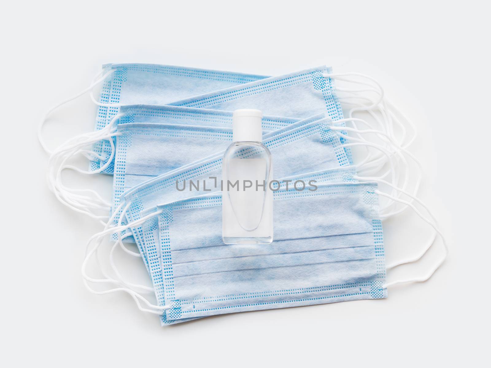 Top view on pack of blue protective medical masks and transparent bottle with sanitizer gel. Coronavirus COVID-19 concept on white background.