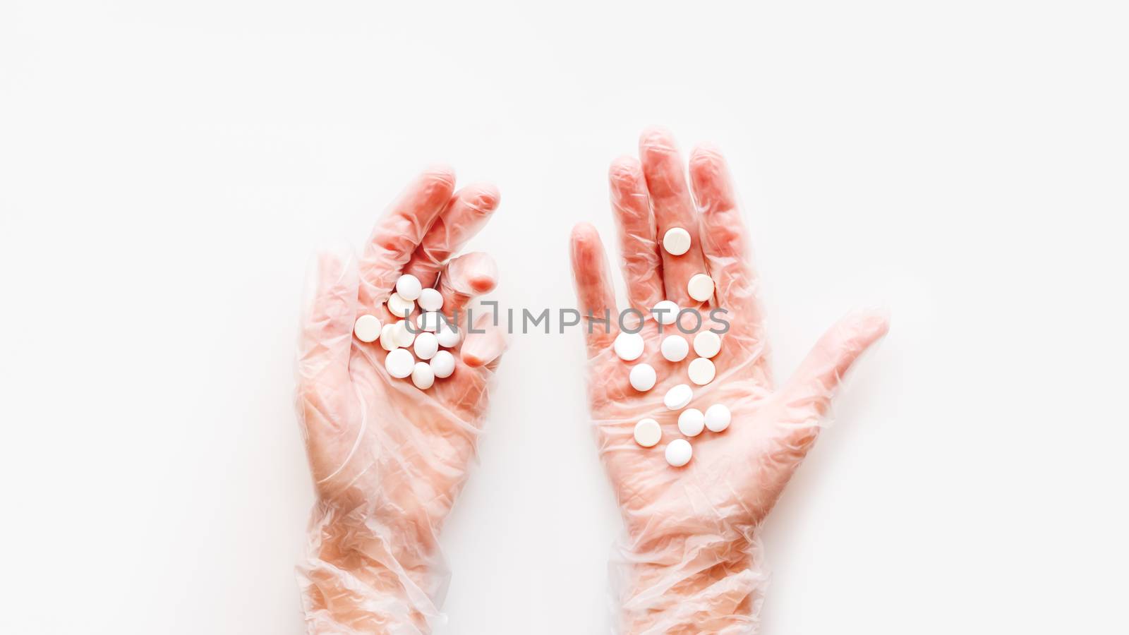 Doctor's palm hands in protective transparent gloves full of white scattering pills. Capsules with medicines on white background with copy space. Flat lay, top view.