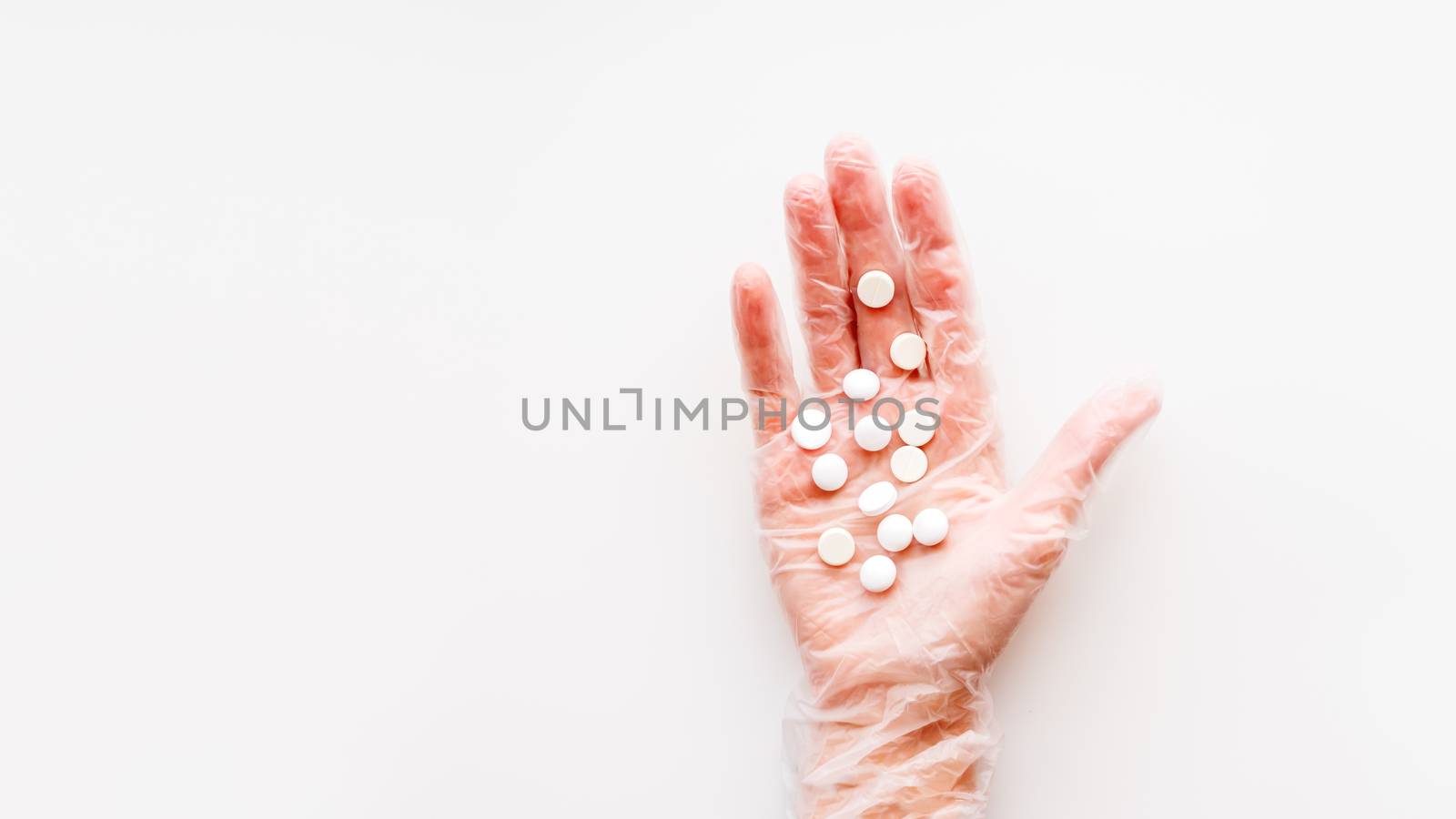 Doctor's palm hand in protective transparent glove full of white scattering pills. Capsules with medicines on white background with copy space. Flat lay, top view.