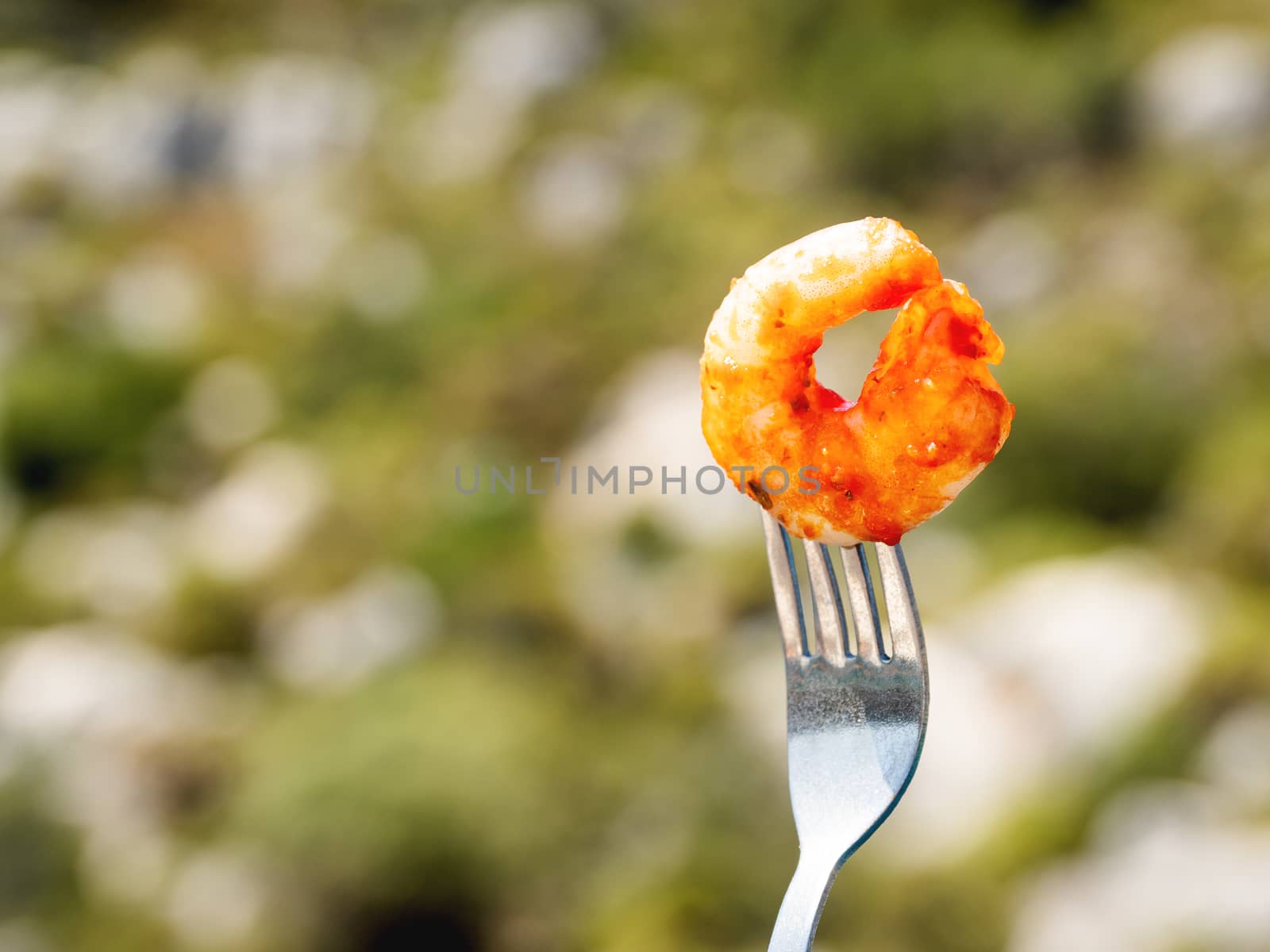 Mediterranean cuisine - freshly roasted shrimp on fork. Seafood on green foliage background. Outdoor picnic. by aksenovko