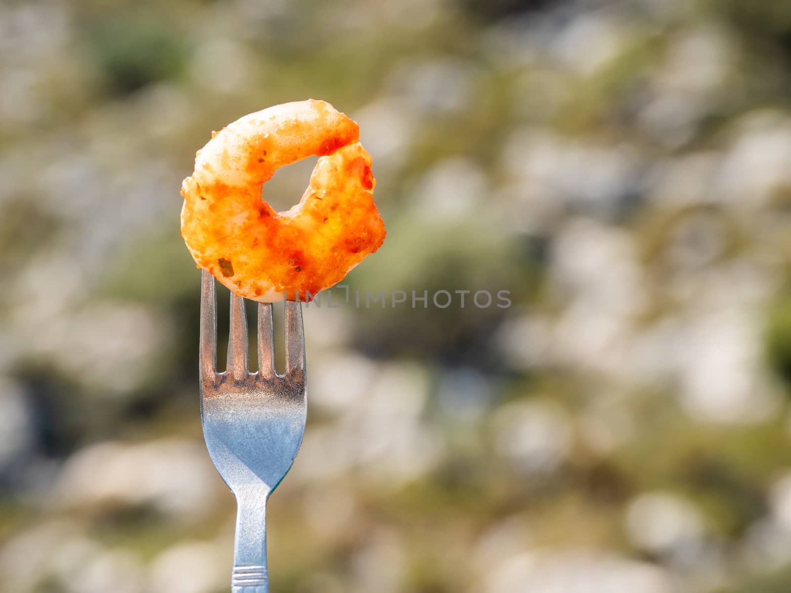 Mediterranean cuisine - freshly roasted shrimp on fork. Seafood on green foliage background. Outdoor picnic.