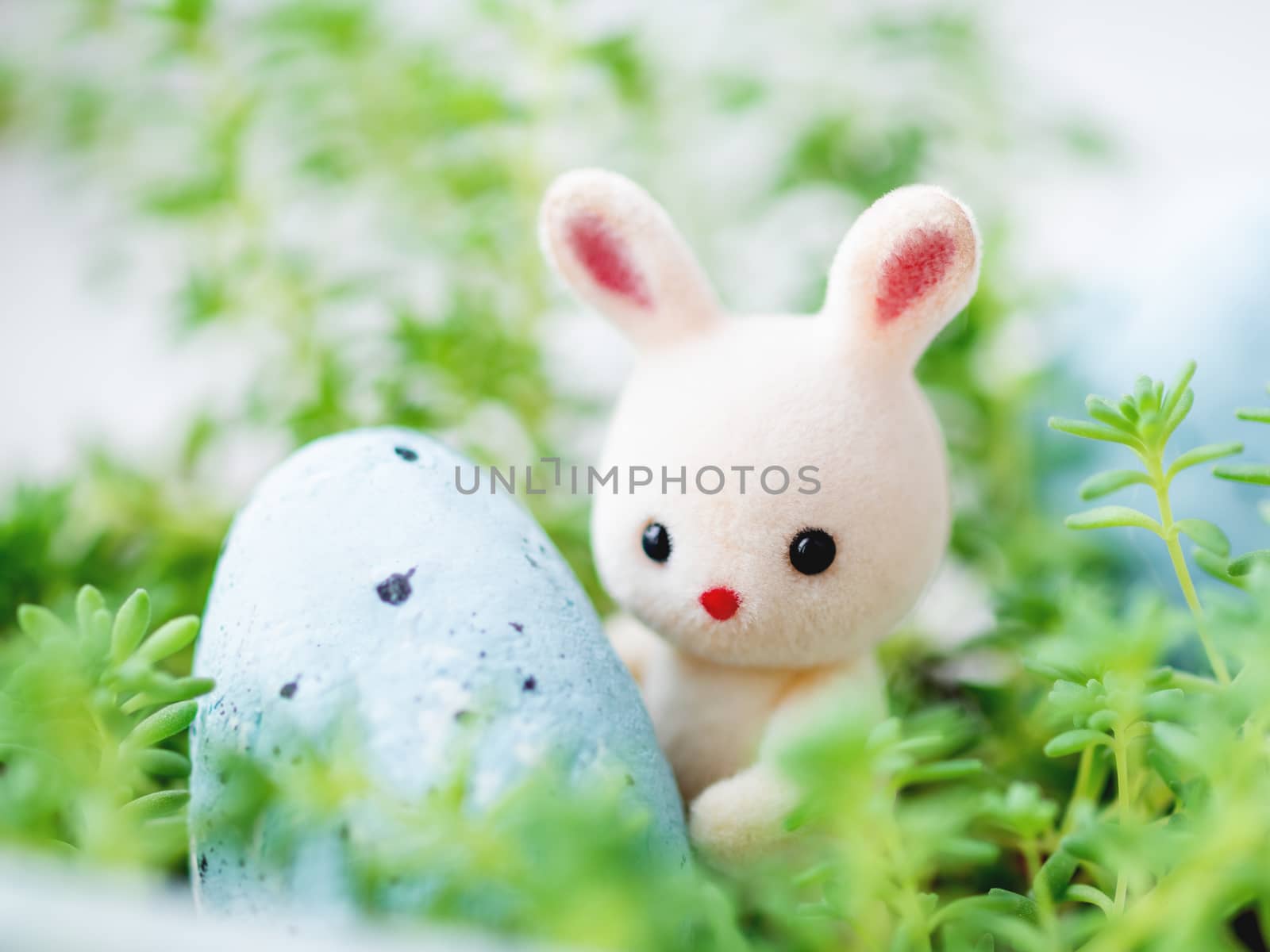 Cute Easter rabbit with light blue egg. Easter celebration concept. White toy bunny in green grass.