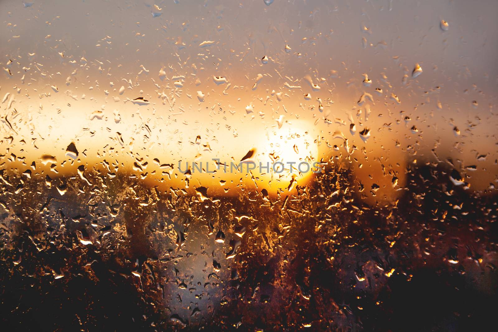 Sunset through window with raindrops after rain. Nature background with bright orange sun beams through wet glass. by aksenovko