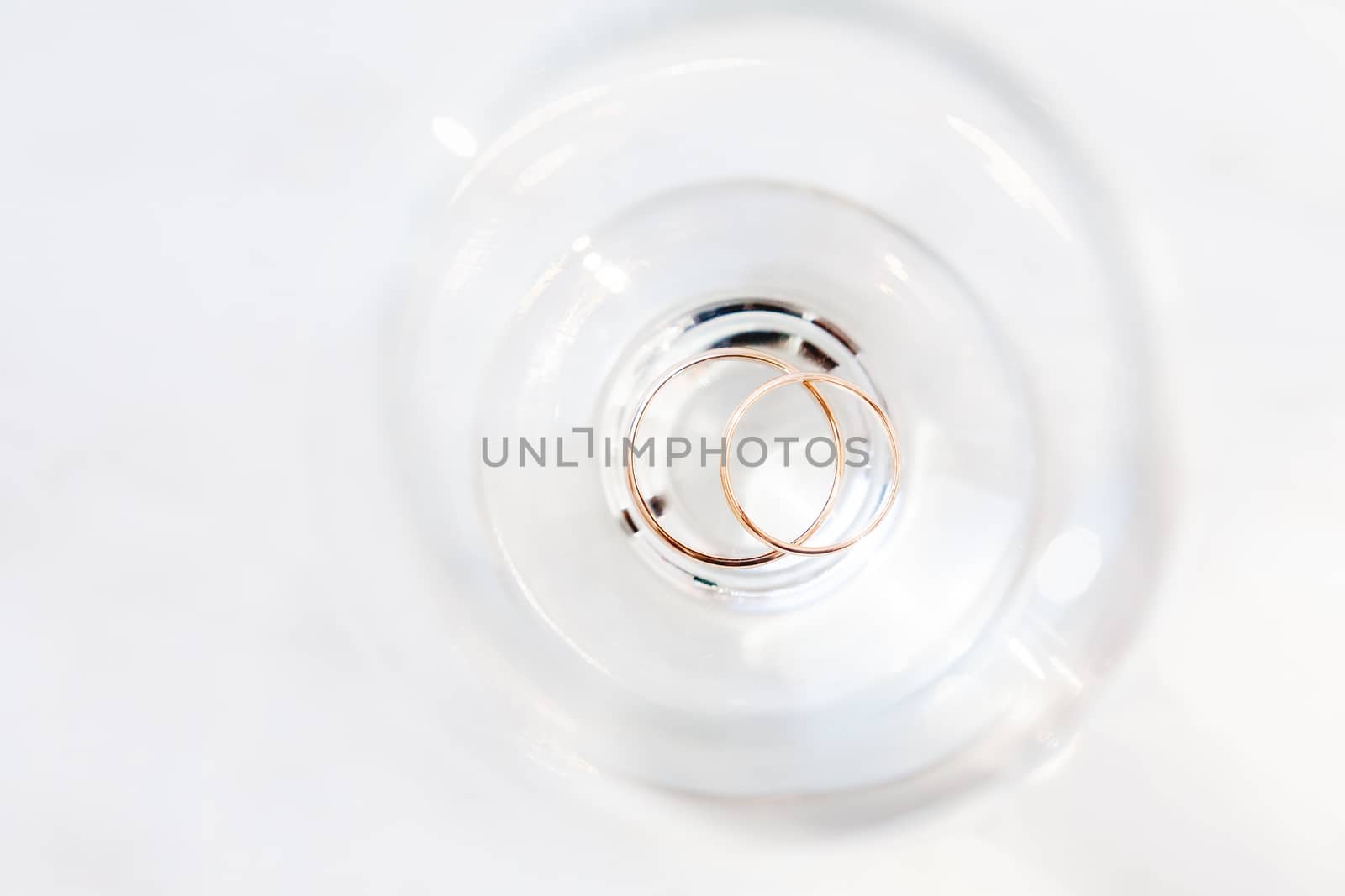 Top view on golden wedding rings inside wine glass. Sun shines through transparent glass.