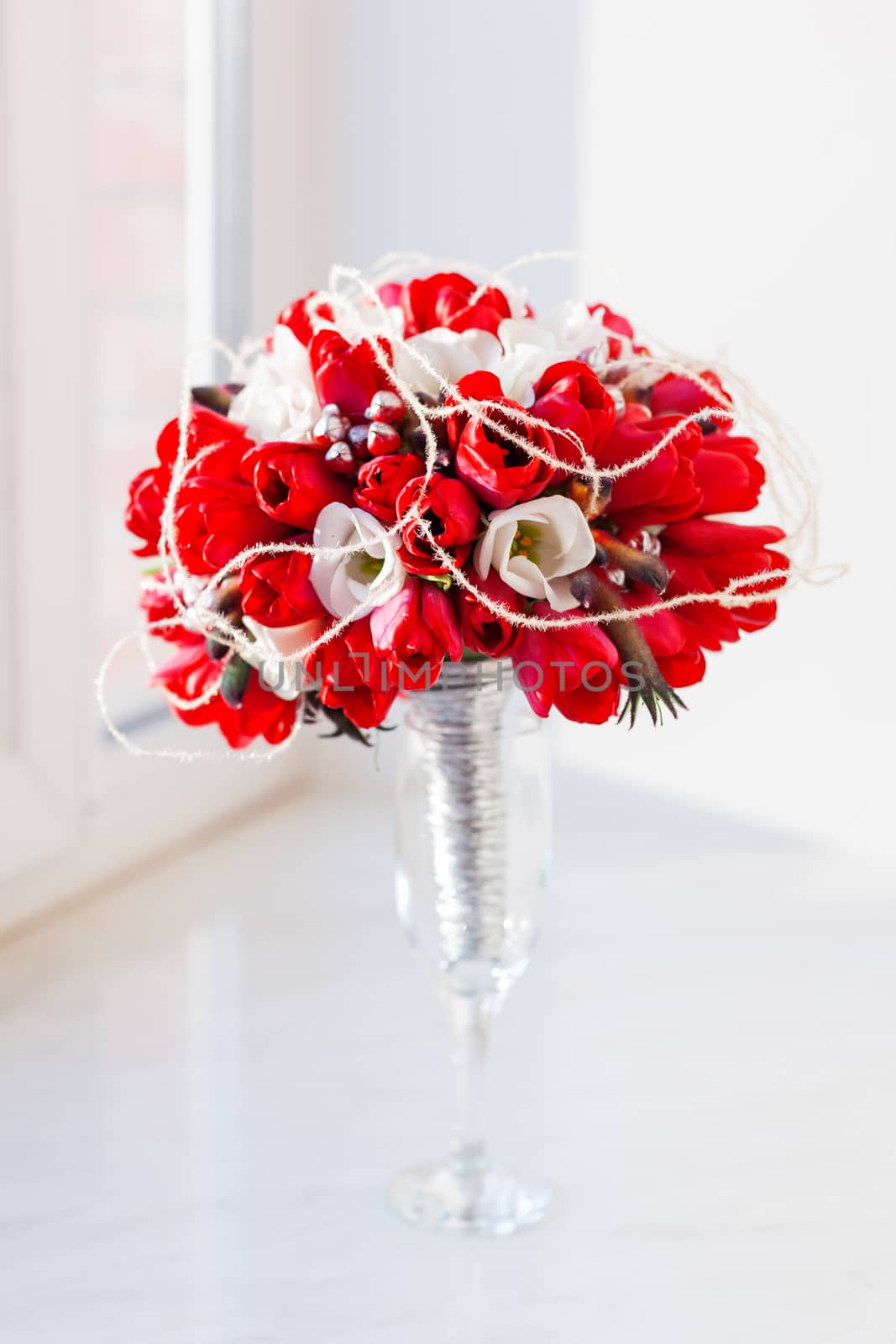 Bridal bouquet in glass vase on sunlight. Traditional floral composition with bright red tulips on window sill.
