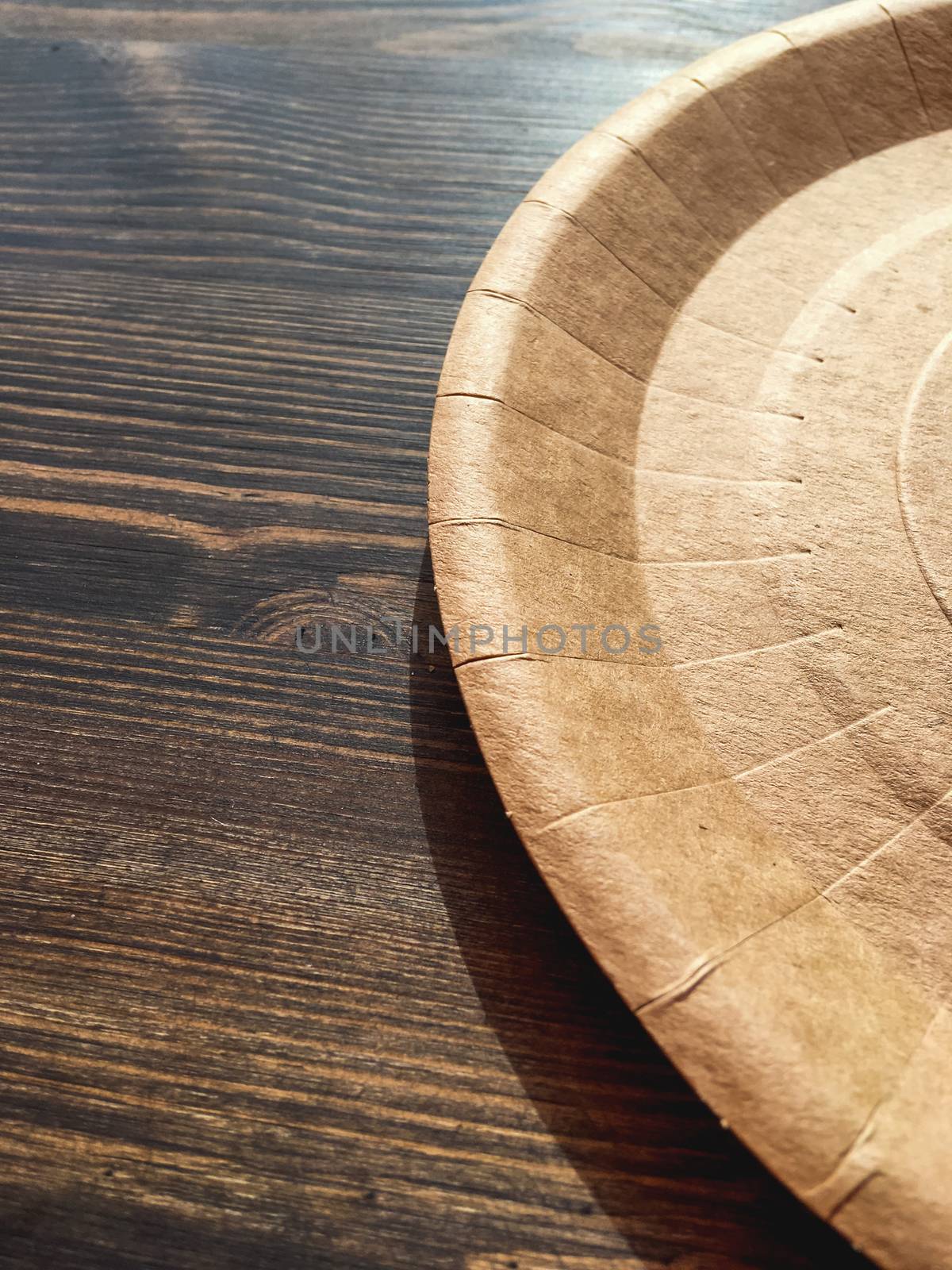 Disposable tableware on wooden table in cafe. Round cardboard plate.
