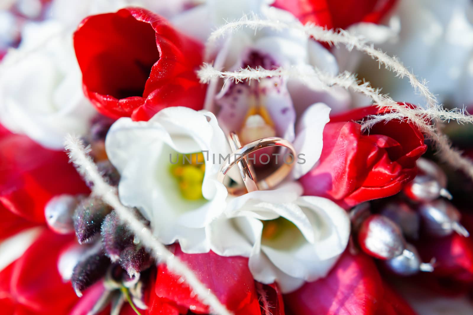 Golden wedding rings on bridal bouquet. Symbol of love and marriage on floral composition of bright red tulips. by aksenovko