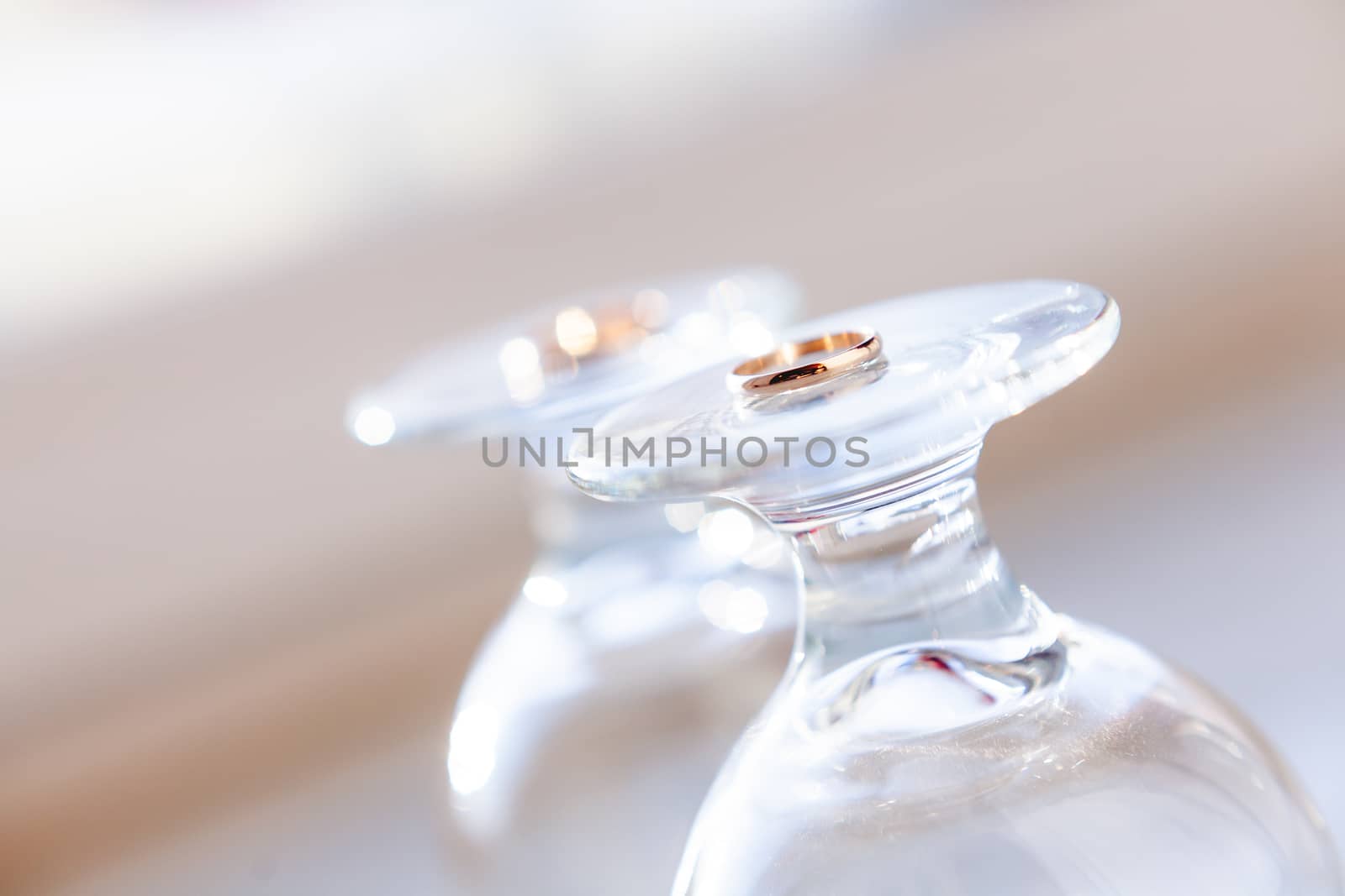 Top view on golden wedding rings lying on top of upside down staying wine glasses. Sun shines through transparent glass. by aksenovko