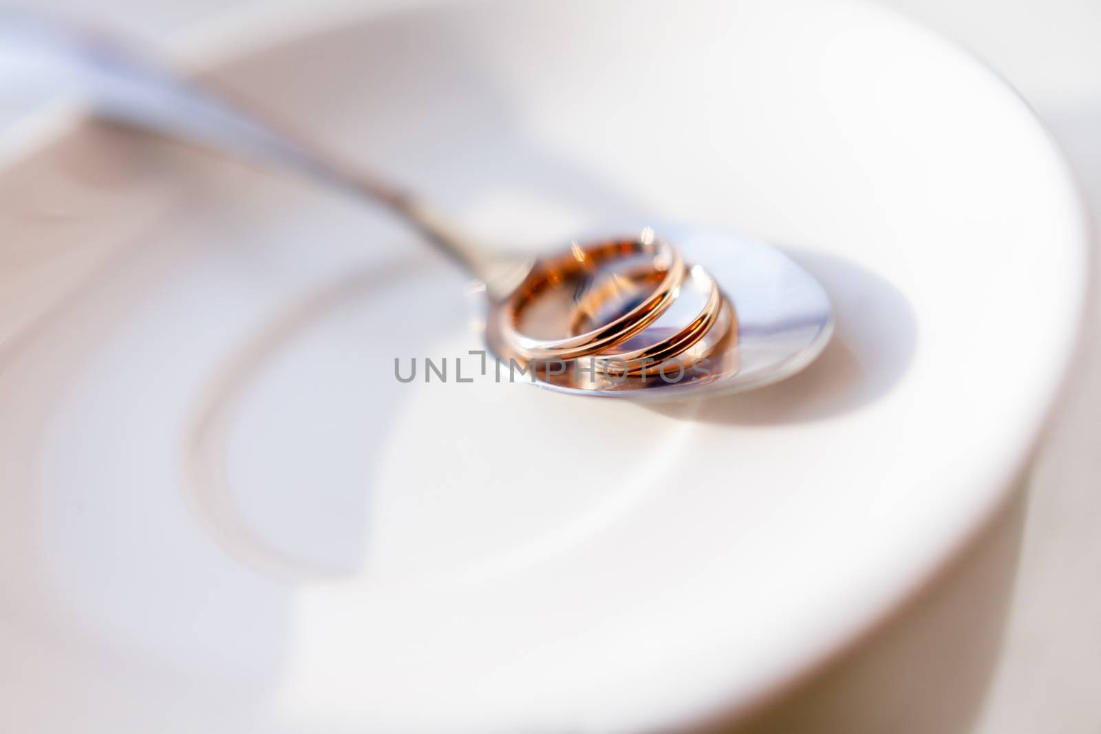 Golden wedding rings on shiny spoon. Traditional symbol of love and marriage on white plate.