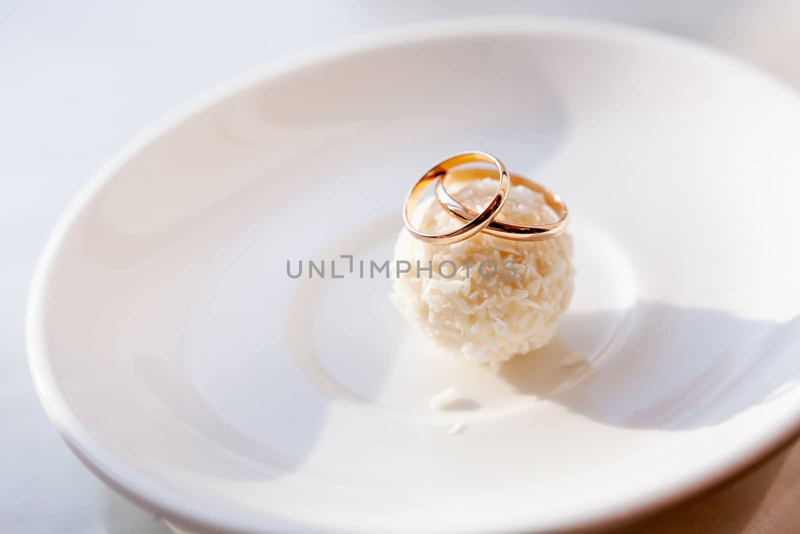 Golden wedding rings on pastry with coconut topping. Traditional symbol of love and marriage on tasty circle tart.