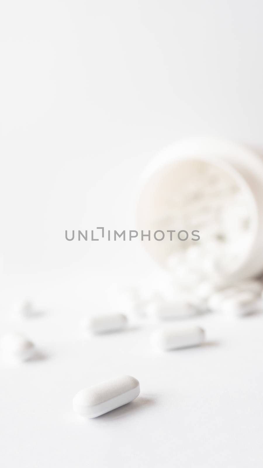 White pills spilled out of a plastic jar. Medicine capsules on white background with copy space.