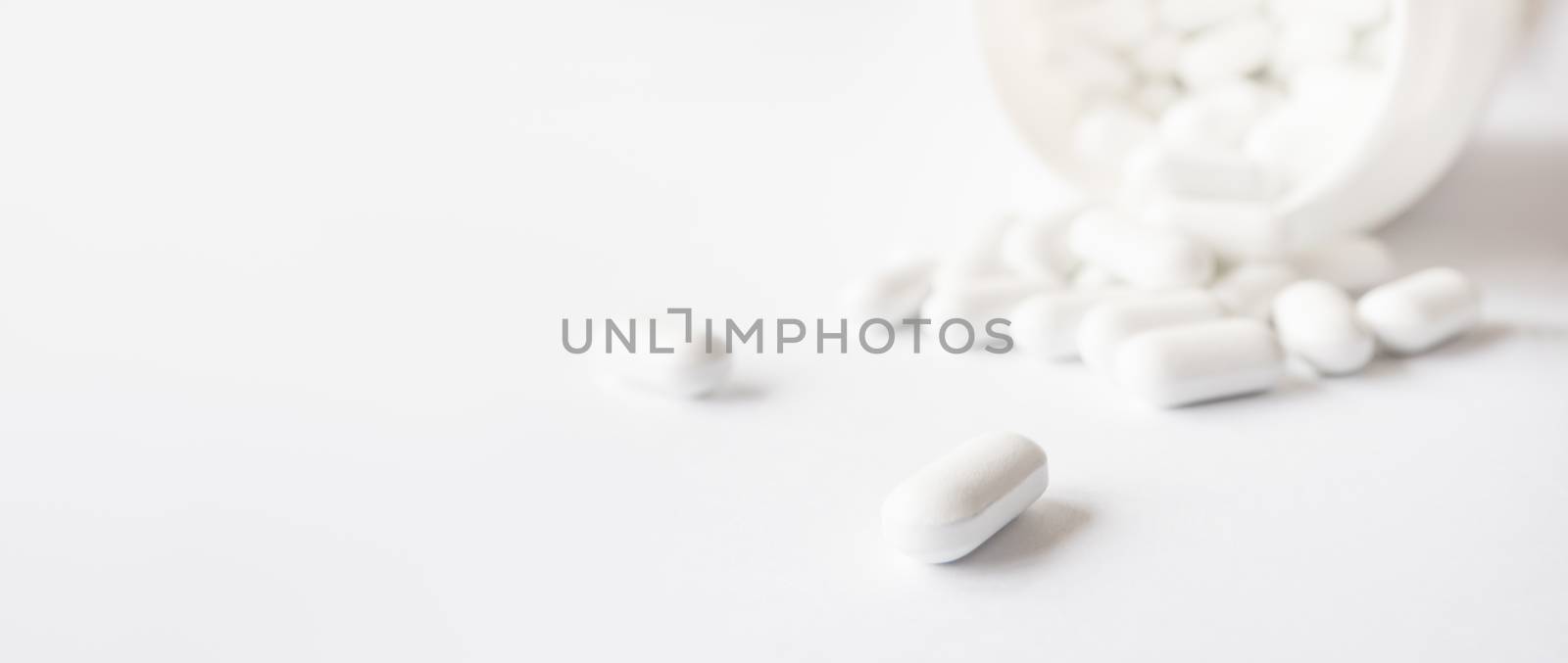 White pills spilled out of a plastic jar. Medicine capsules on white background with copy space.