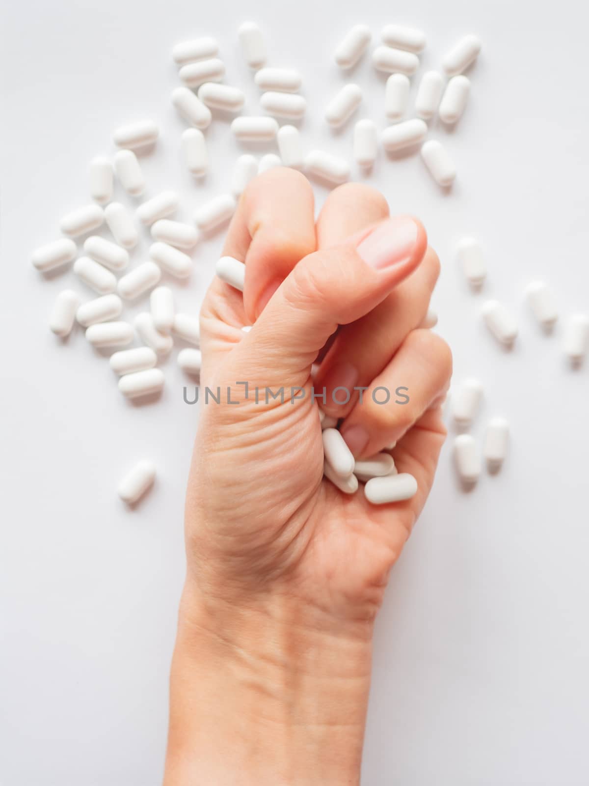 Palm hand full of white scattering pills. Woman gripes hand with capsules with medicines on light background. Flat lay, top view.