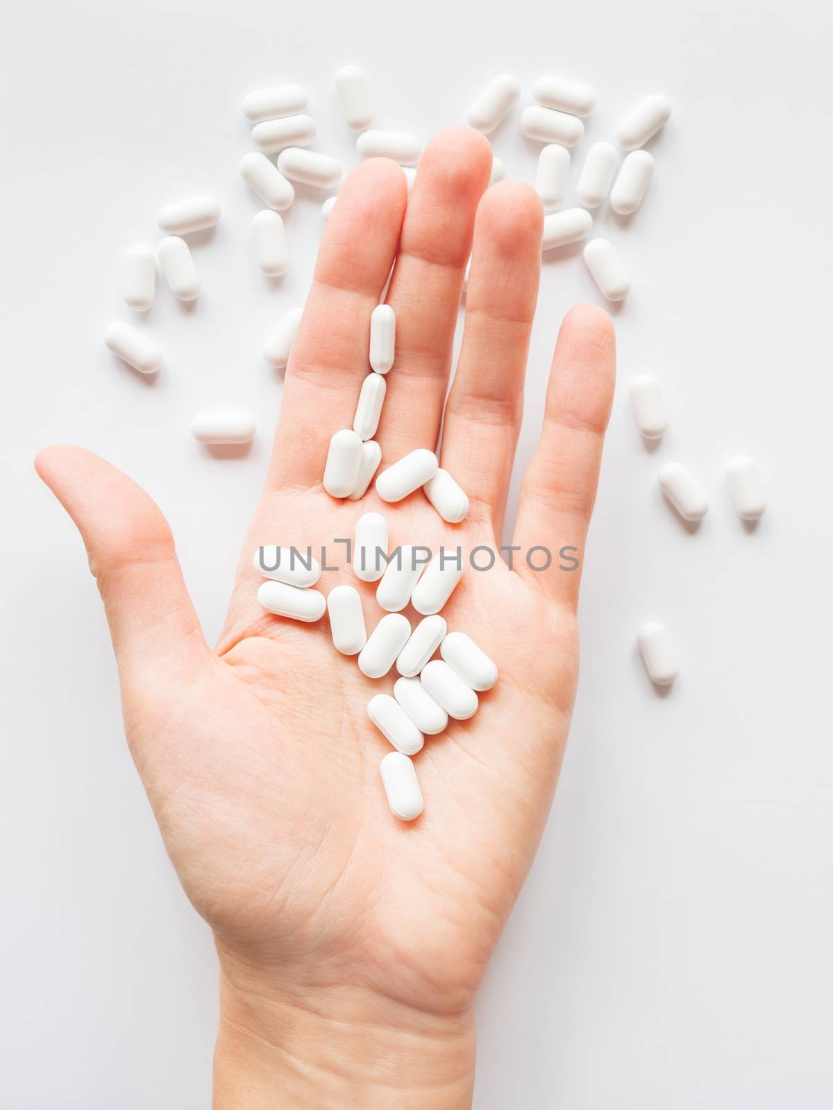 Palm hand full of white scattering pills. Capsules with medicines on light background. Flat lay, top view. by aksenovko