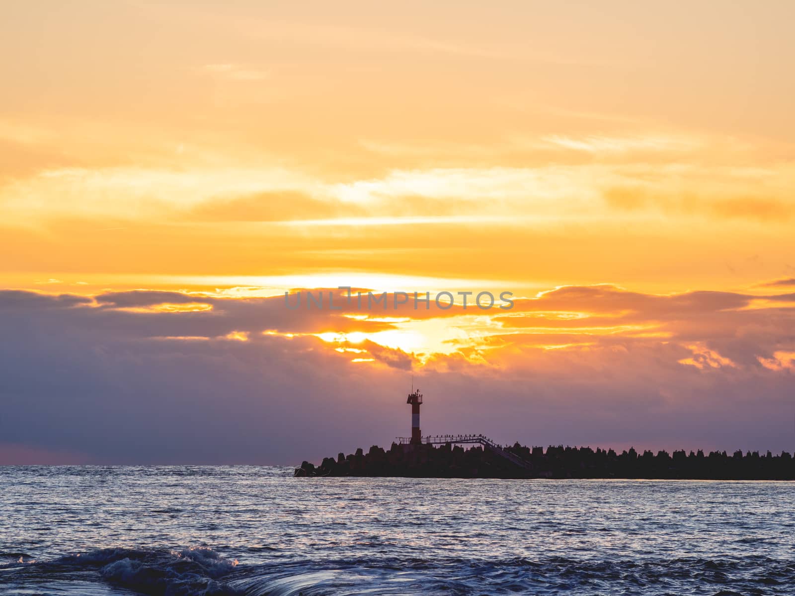 Beautiful sunset over Black sea in Sochi, Russia. Silhouettes of lighthouse and seagulls on the railing. by aksenovko
