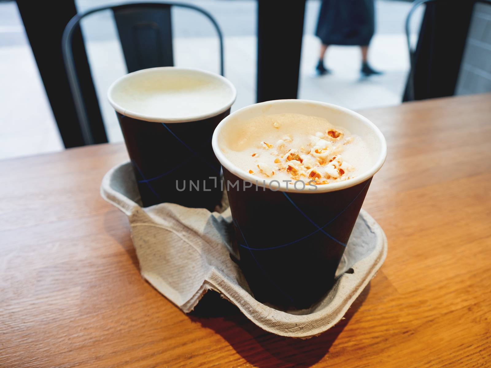 Two paper cups with tasty coffee on wooden table in cafe.. Hot beverage with popcorn on frothy milk. Holder made from recycled cardboard for both cups.