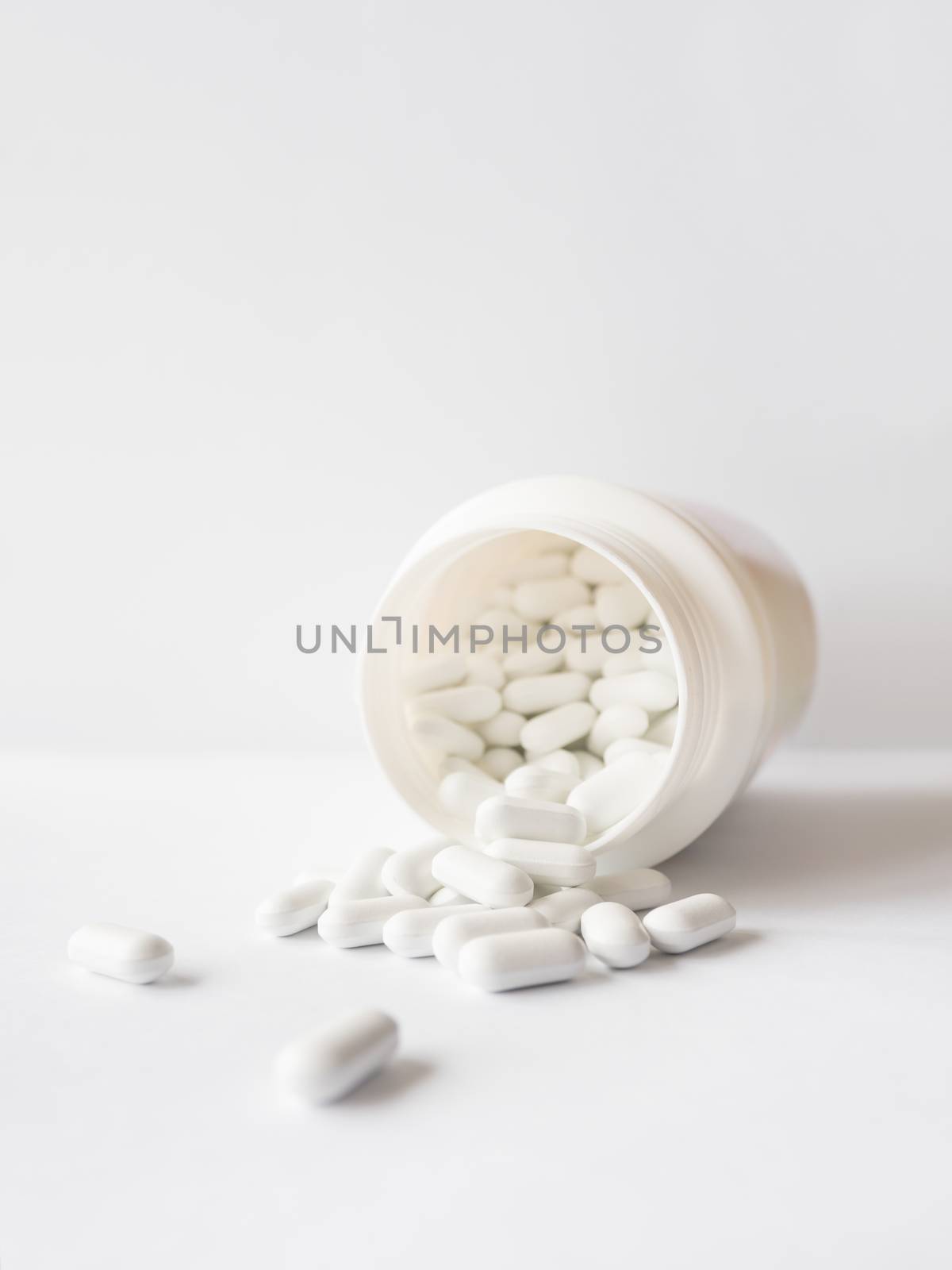 White pills spilled out of a plastic jar. Medicine capsules on white background with copy space.