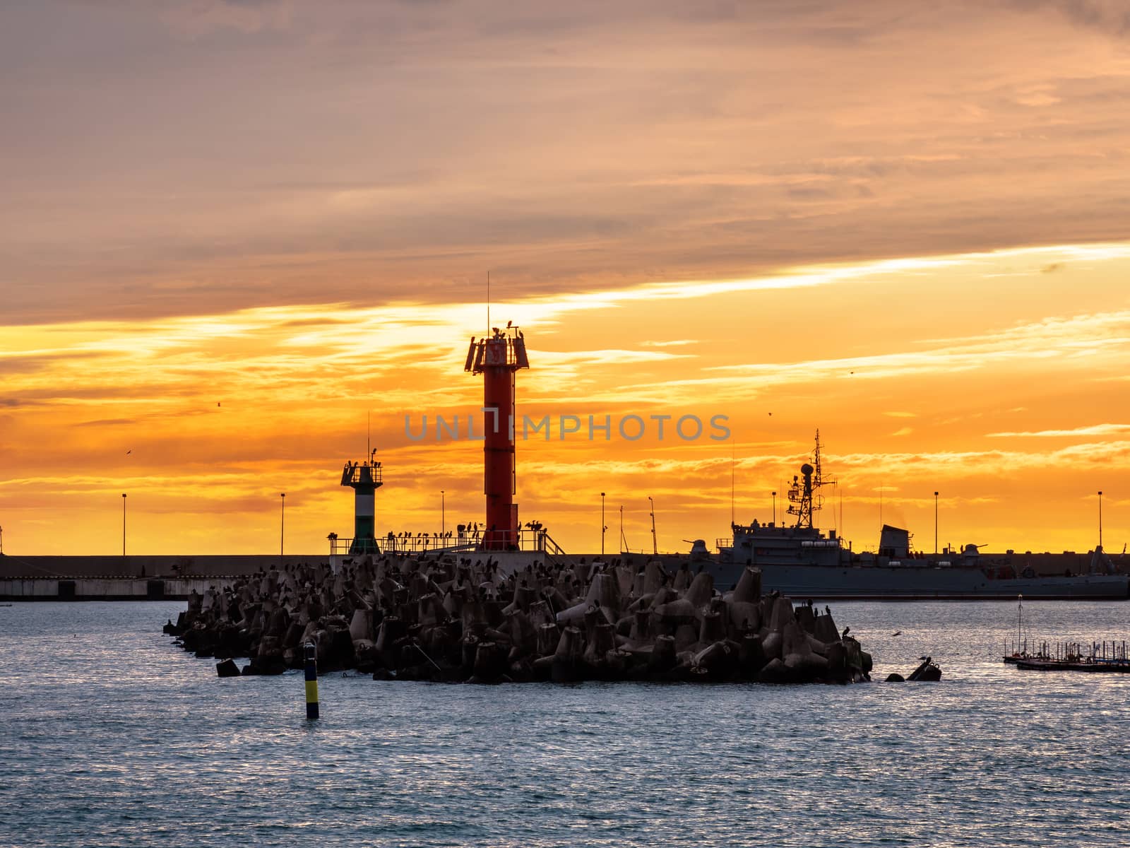 Beautiful sunset over Black sea and lighthouse in port of Sochi, Russia. Silhouettes of seagulls on rocks and tranquil sea surf.