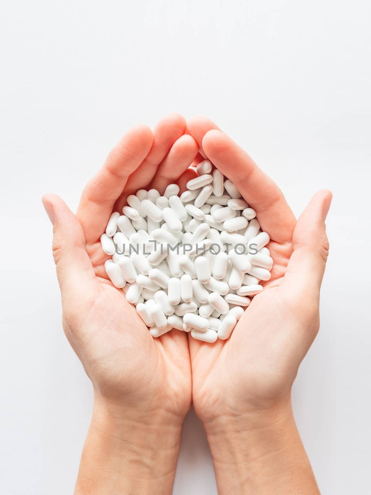 Palm hands full of white scattering pills. Woman gripes hand with capsules with medicines on light background. Flat lay, top view.