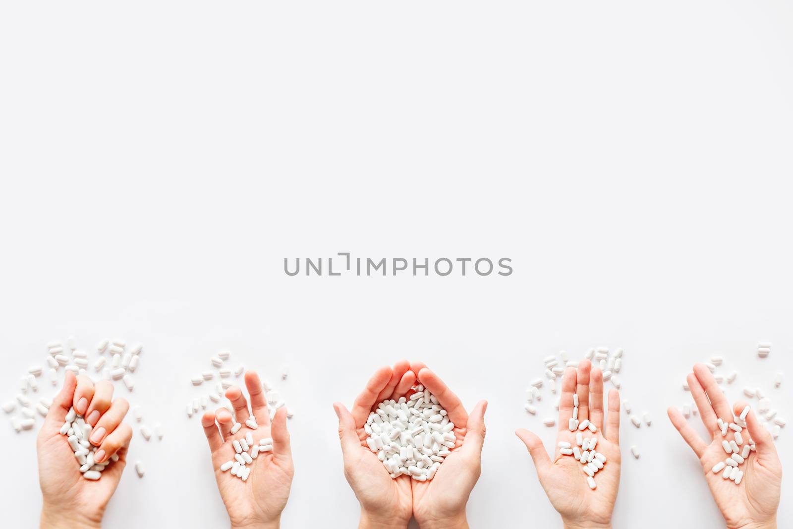 Palm hands full of white scattering pills. Woman gripes hand with capsules with medicines on light background. Flat lay, top view.