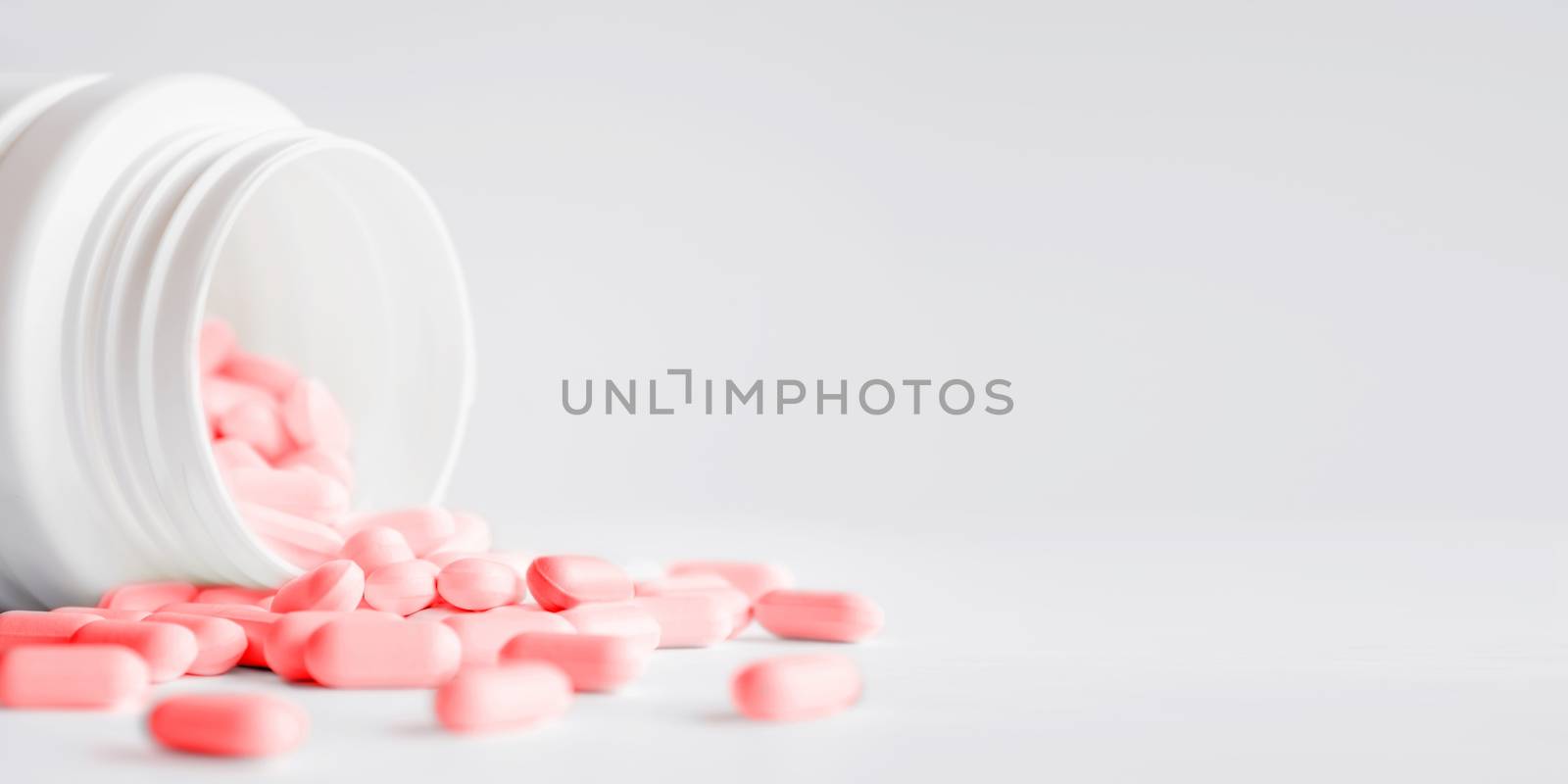 Pink pills with spilled out of a plastic jar. Medicine capsules on white background with copy space.