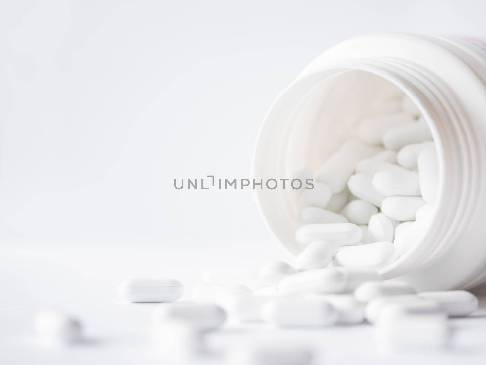 White pills spilled out of a plastic jar. Medicine capsules on white background with copy space.