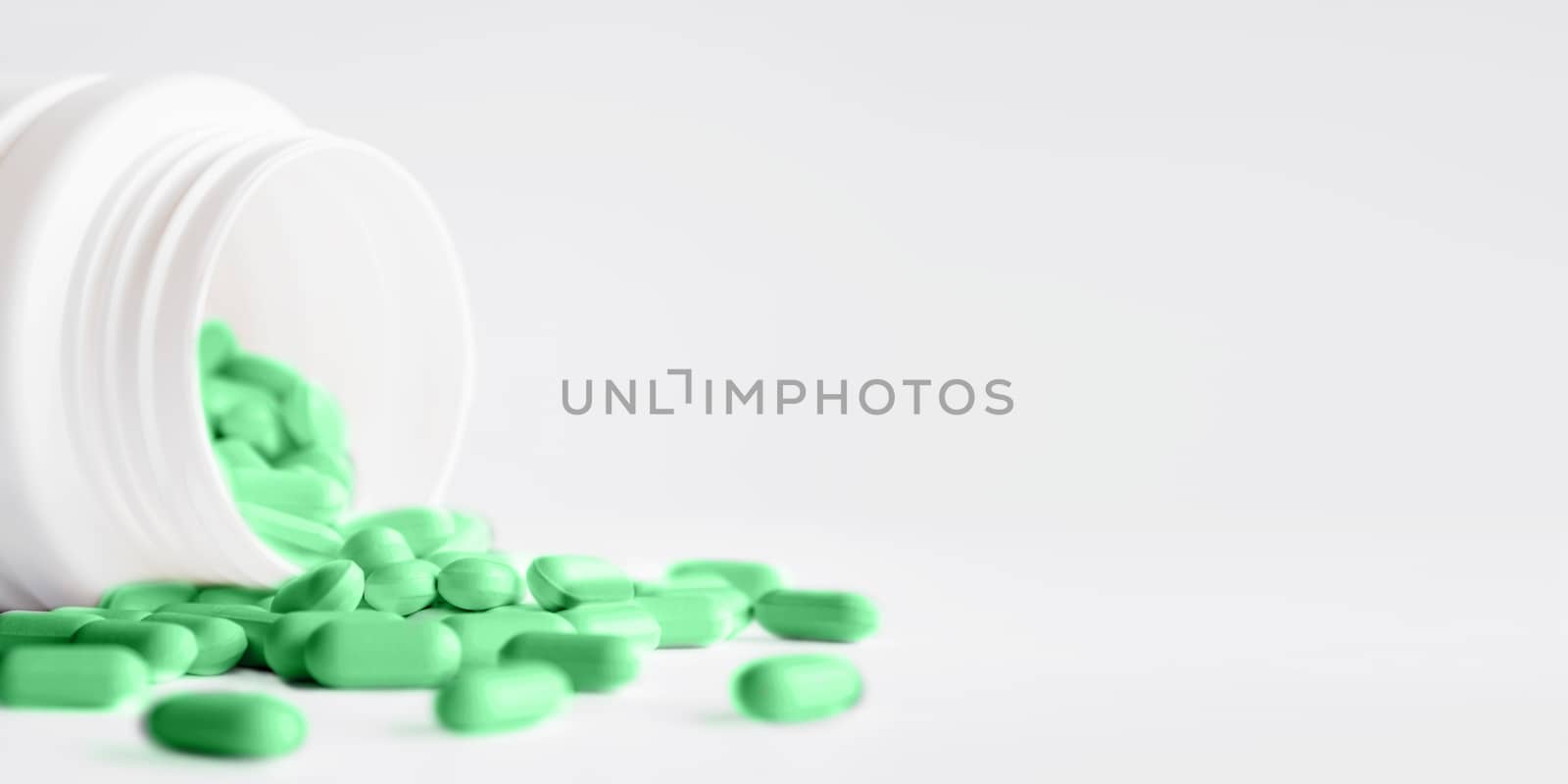 Green pills with spilled out of a plastic jar. Medicine capsules on white background with copy space.