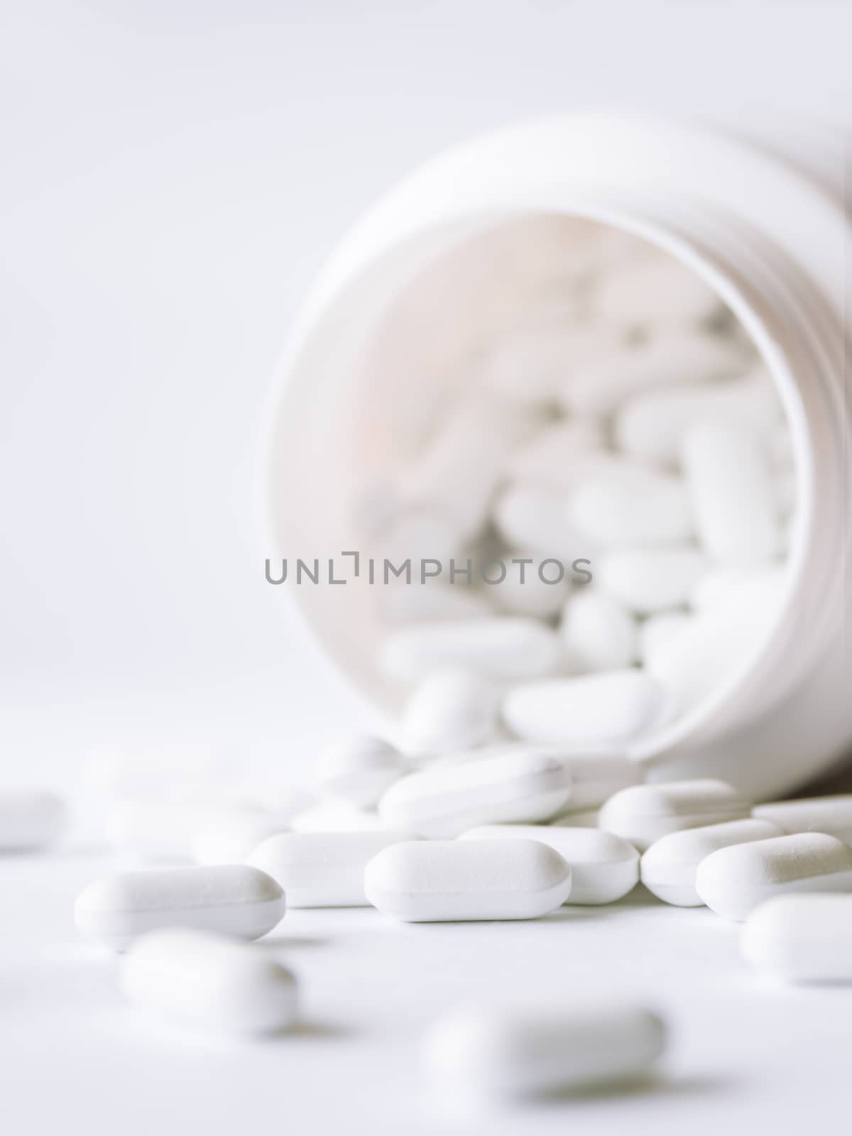 White pills spilled out of a plastic jar. Medicine capsules on white background.