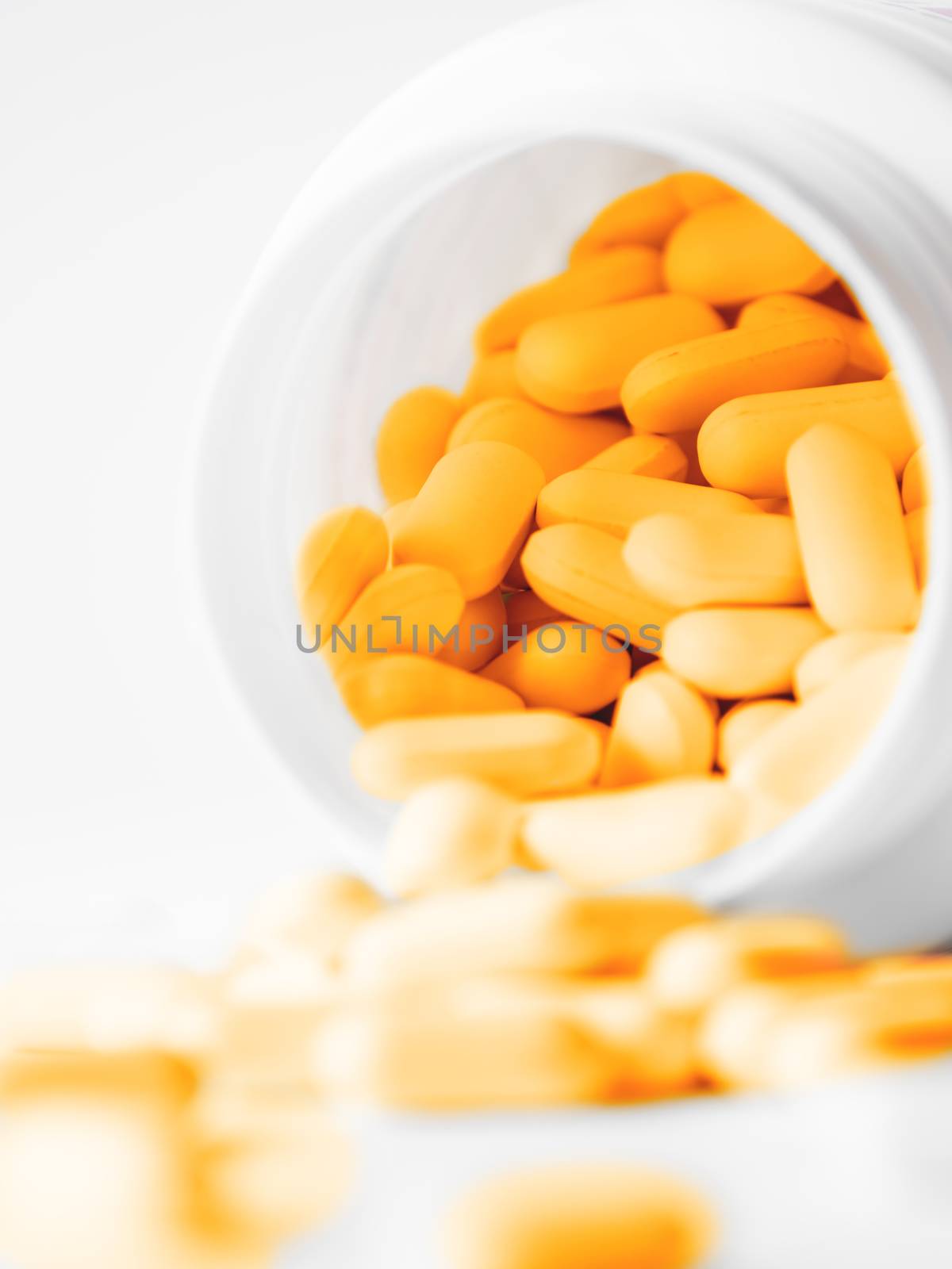 Orange pills spilled out of a plastic jar. Medicine capsules on white background.