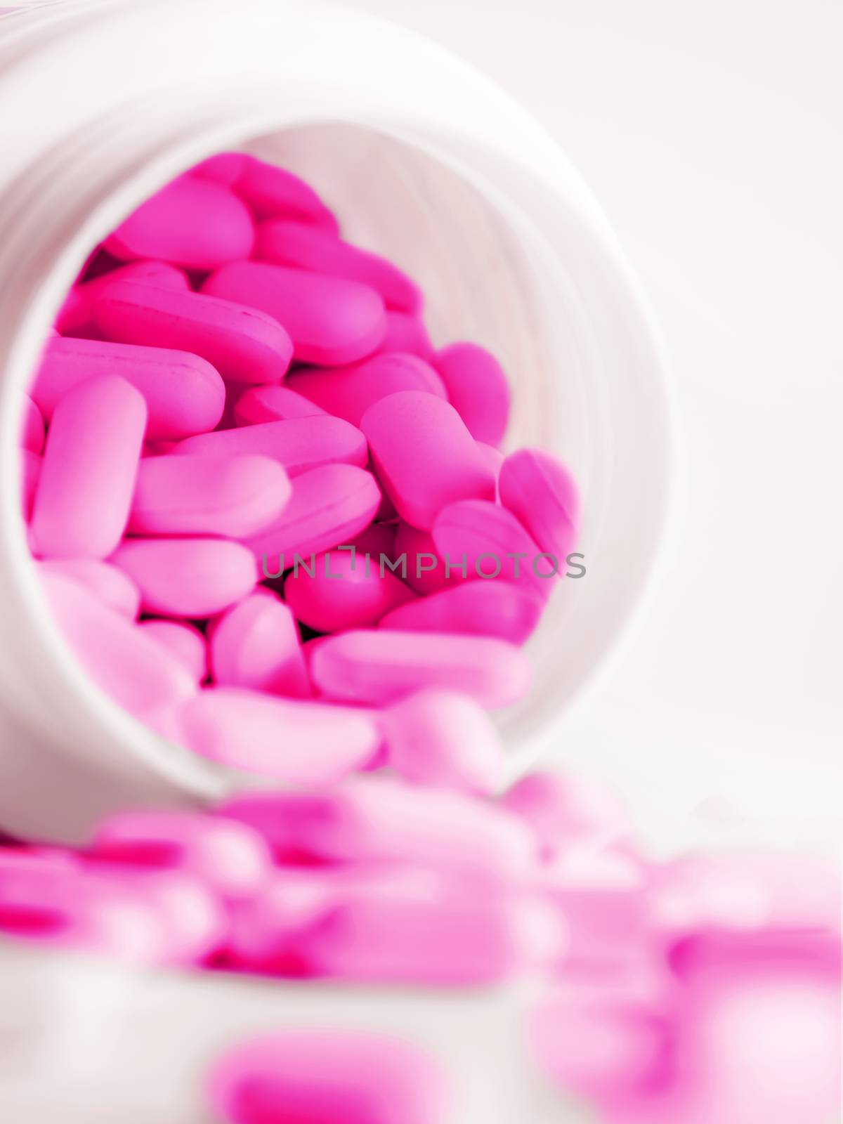 Purple pills spilled out of a plastic jar. Medicine capsules on white background.