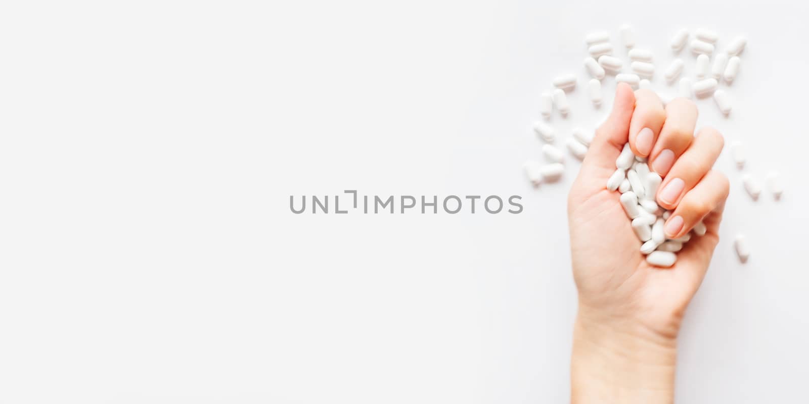 Palm hand full of white scattering pills. Woman gripes hand with capsules with medicines on light background. Flat lay, top view. Banner with copy space. by aksenovko