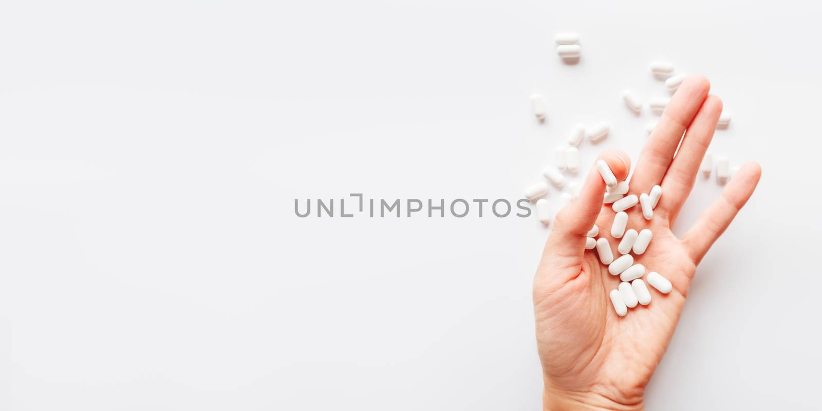 Palm hand full of white scattering pills. Capsules with medicines on light background. Flat lay, top view.