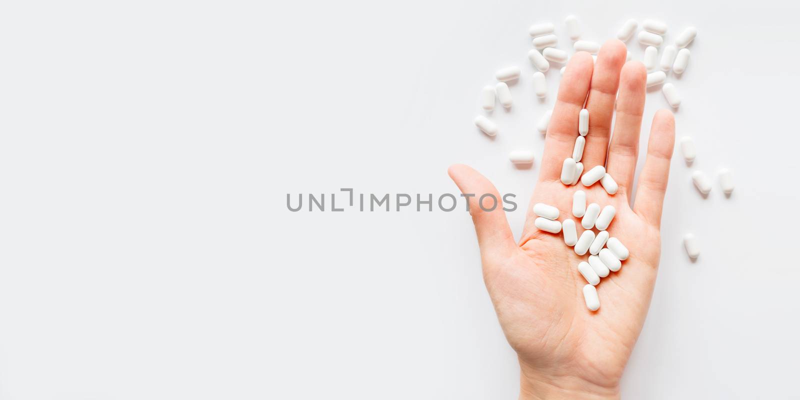 Palm hand full of white scattering pills. Capsules with medicines on light background. Flat lay, top view.