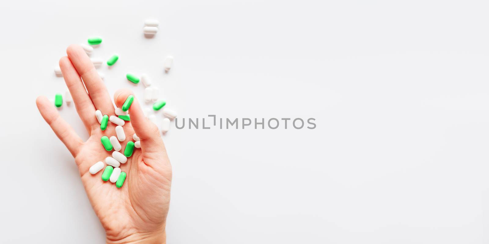 Palm hand full of white and green scattering pills. Capsules with medicines on light background. Flat lay, top view.