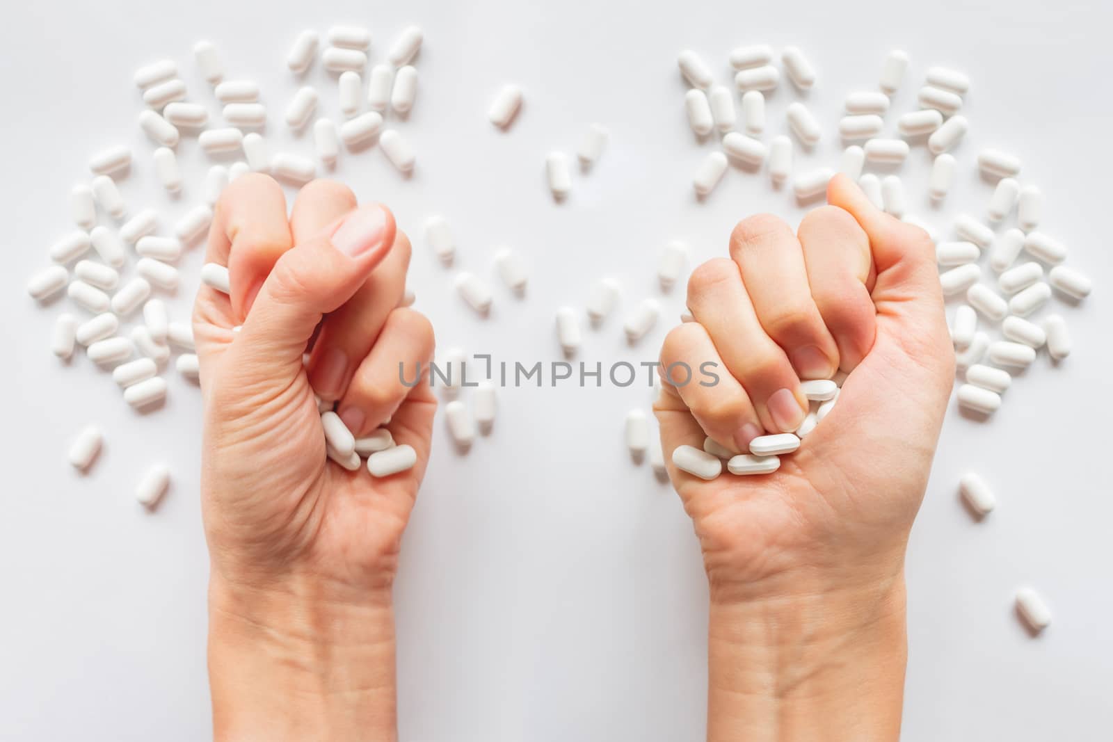 Palm hands full of white scattering pills. Woman gripes hand with capsules with medicines on light background. Flat lay, top view.