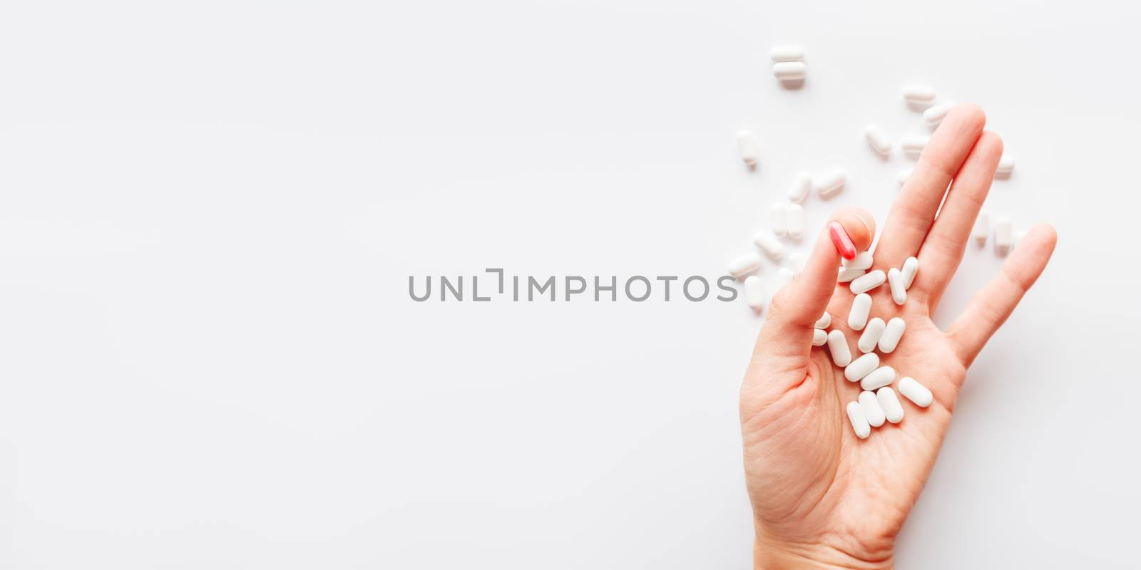 Palm hand full of white and red one scattering pills. Capsules with medicines on light background. Flat lay, top view.