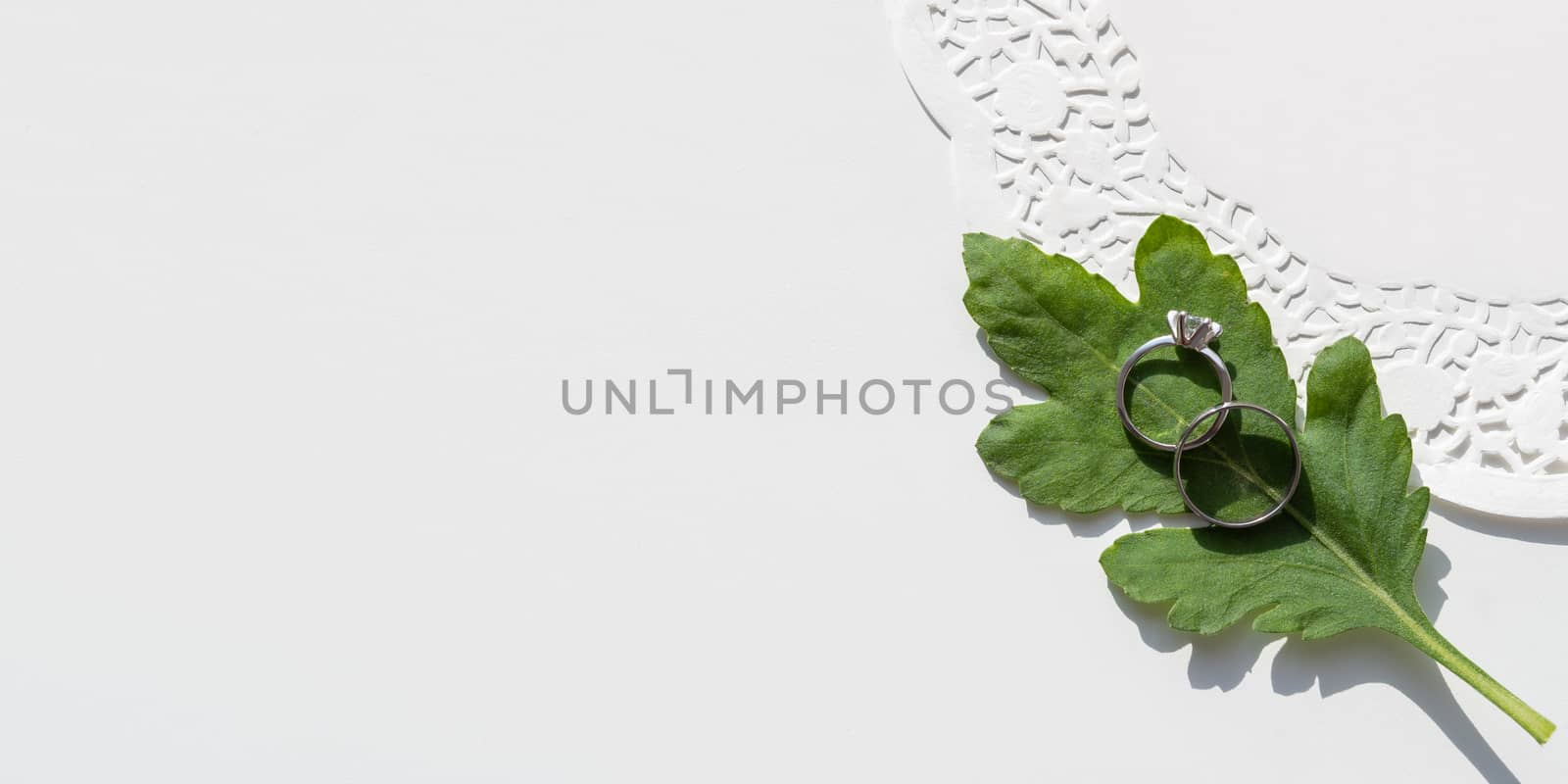 Top view on two wedding rings on green leaf. Plant with traditional jewelry accessories with laces napkin. White background with copy space.