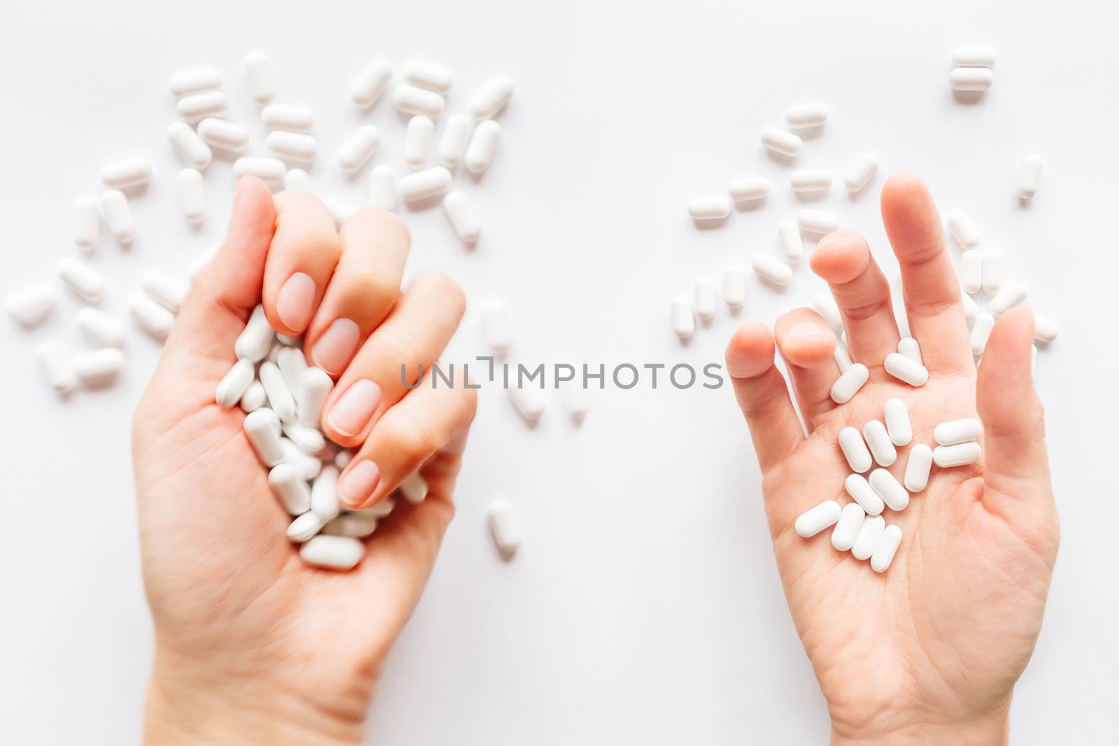 Palm hands full of white scattering pills. Woman gripes hand with capsules with medicines on light background. Flat lay, top view.