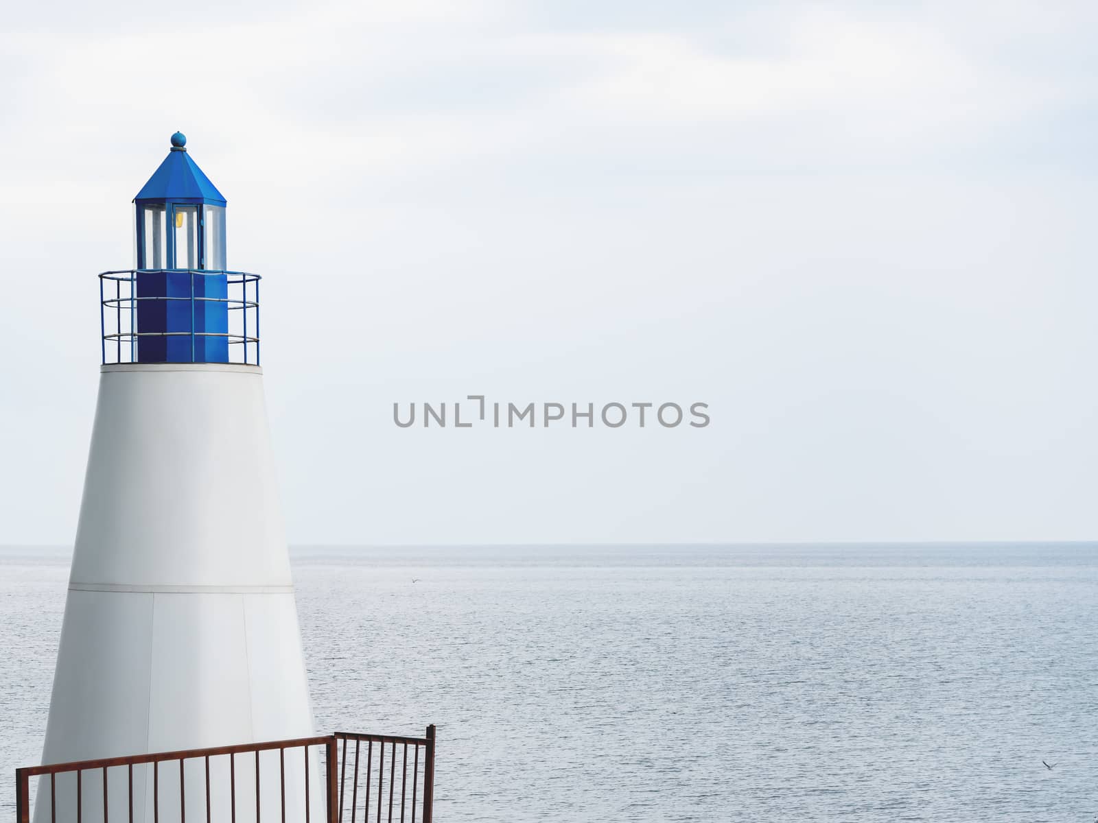 White lighthouse with blue tower on grey tranquil sea background. Natural background with copy space.