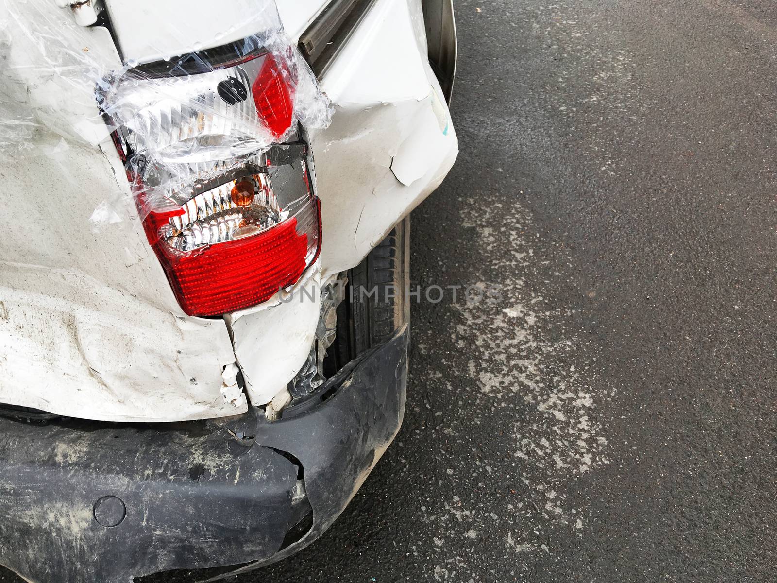 Car after the accident. Broken bumper and headlight. White car with dents covered with plastic wrap.