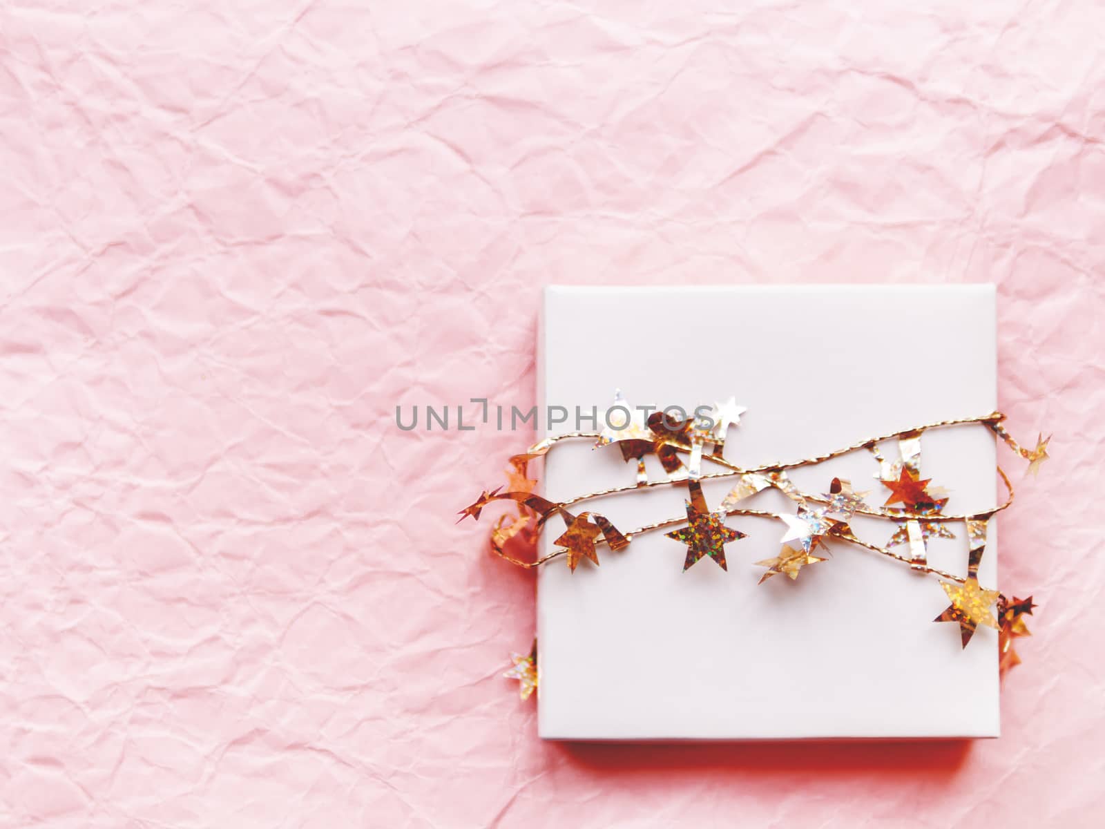 Valentine's Day present in a white box with golden stars ribbon. Gift box on pink crumpled paper background with copy space.