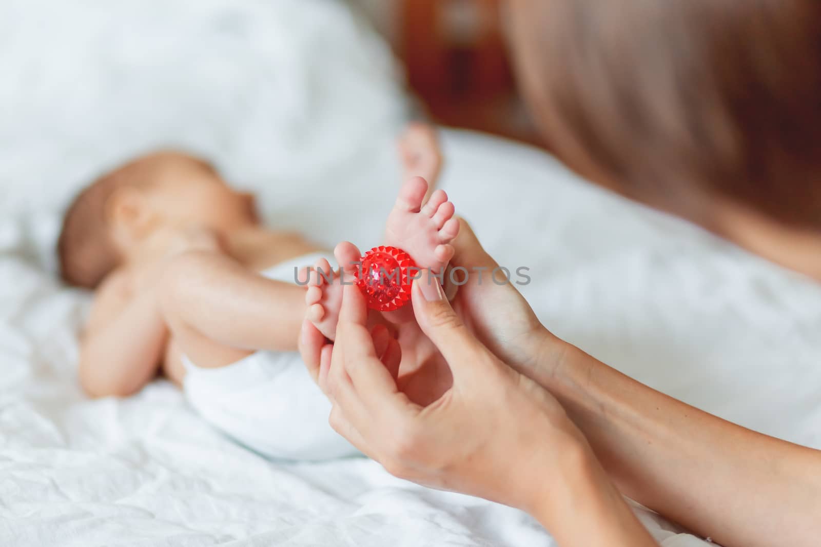 Mother holds newborn baby's feet. Tiny fingers and red massage ball in woman's hand. Cozy morning at home. by aksenovko