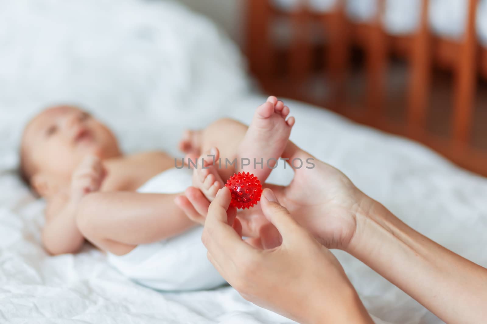 Mother holds newborn baby's feet. Tiny fingers and red massage ball in woman's hand. Cozy morning at home. by aksenovko