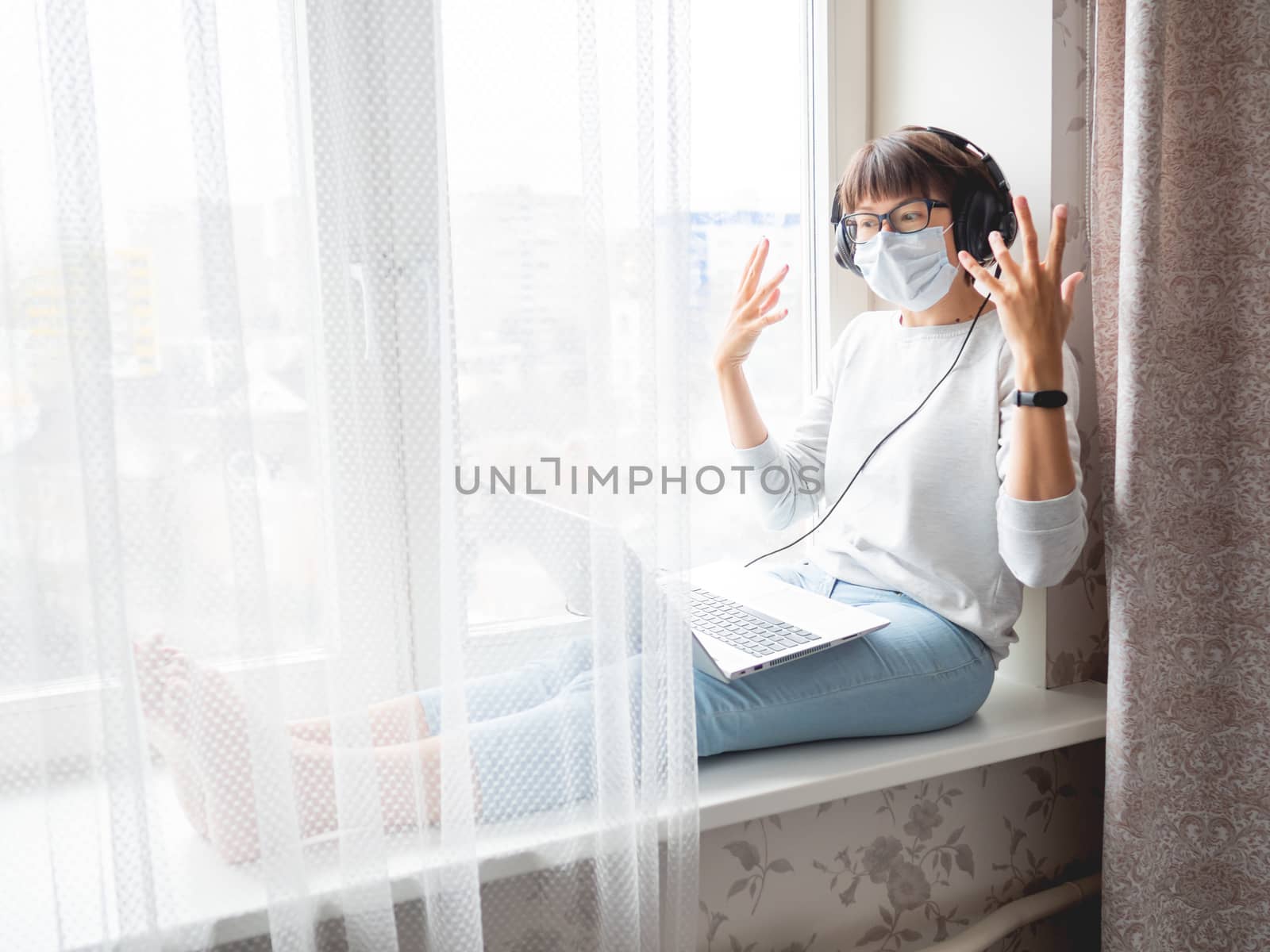 Woman in medical mask remote works from home. She speaks online by aksenovko