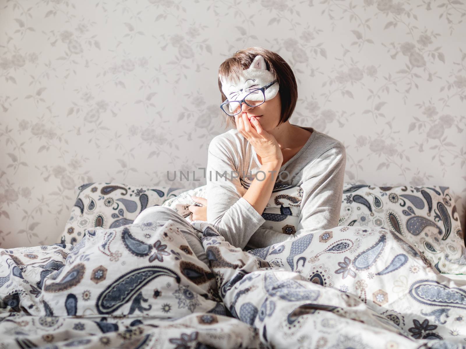 Young woman in grey pajama, glasses and sleeping mask in shape o by aksenovko