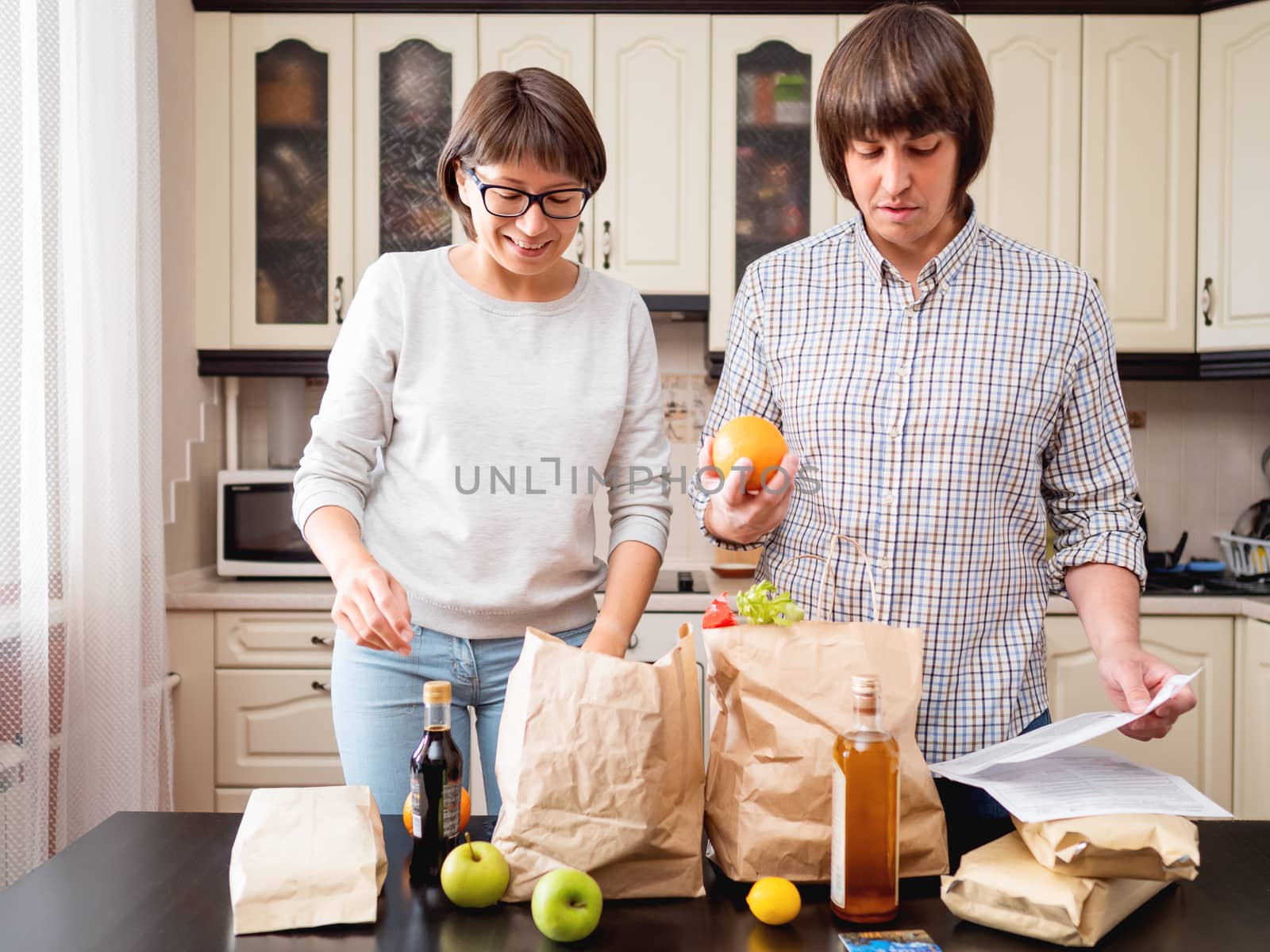 Young couple is sorting out purchases in the kitchen. Products in bags made of craft paper. Food delivery in conditions of quarantine because of coronavirus COVID19.