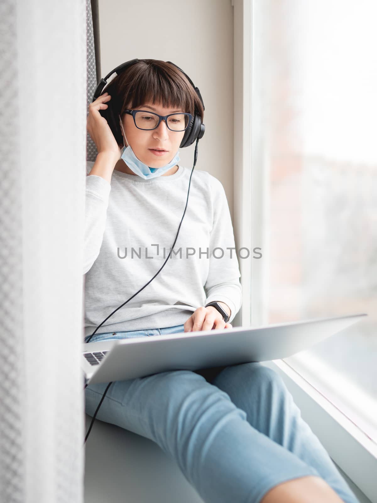 Woman in medical mask remote works from home. She sits on window by aksenovko