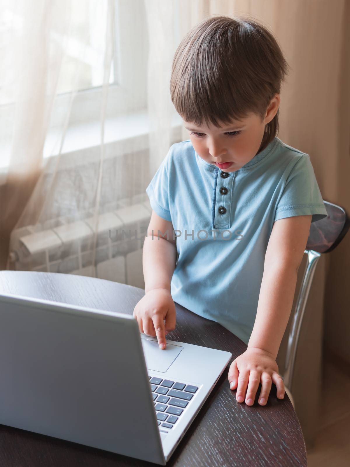 Curious toddler boy explores the laptop and presses buttons on computer keyboard.
